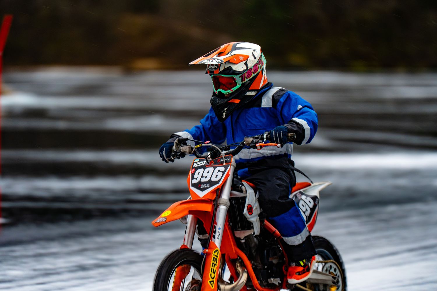Dirt bike rider in blue jersey and orange KTM motorcycle racing on wet track in motion.
