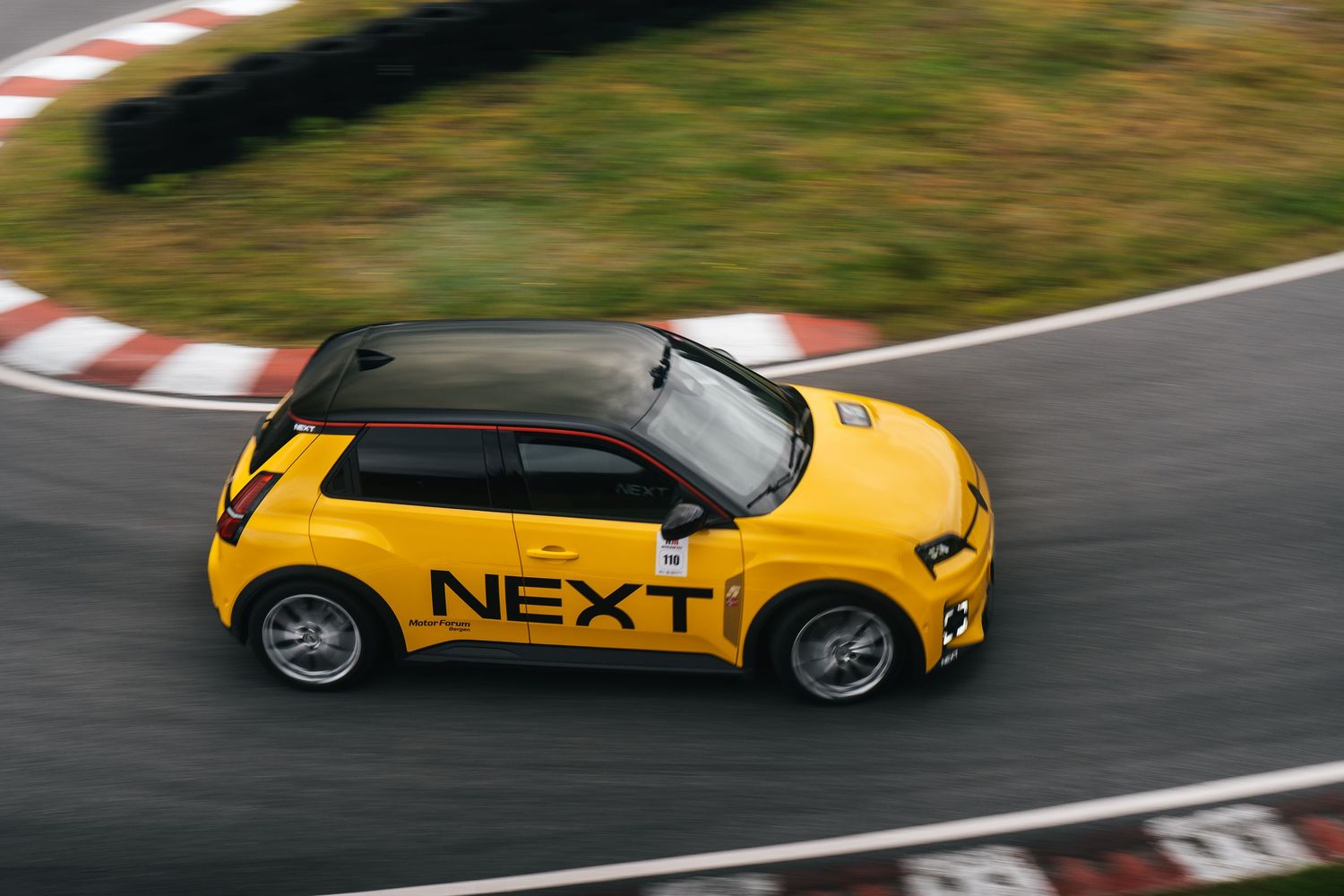 Yellow sports car races around a curved racetrack during a cloudy day.