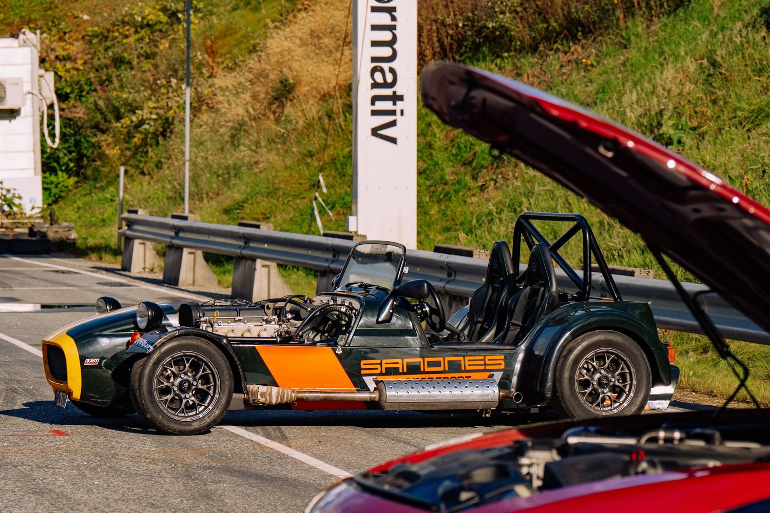 A black and orange race car chassis with exposed mechanical components parked on a road.