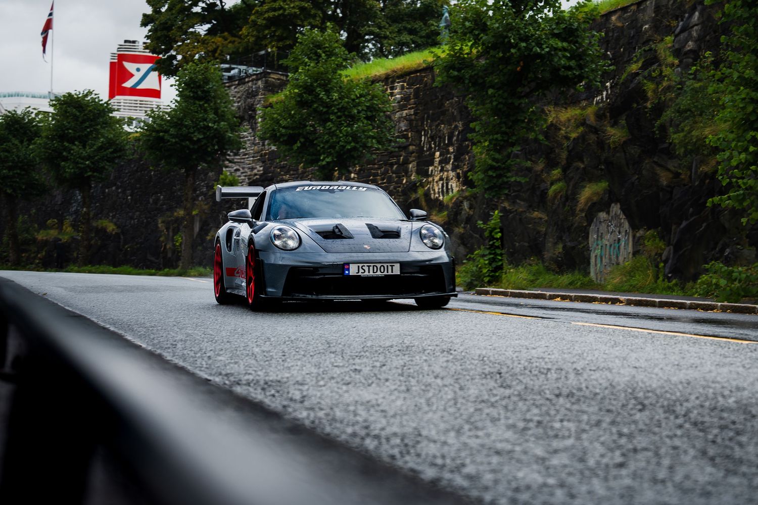 Luxury vehicles lined up on curved mountain road with lush greenery in background.