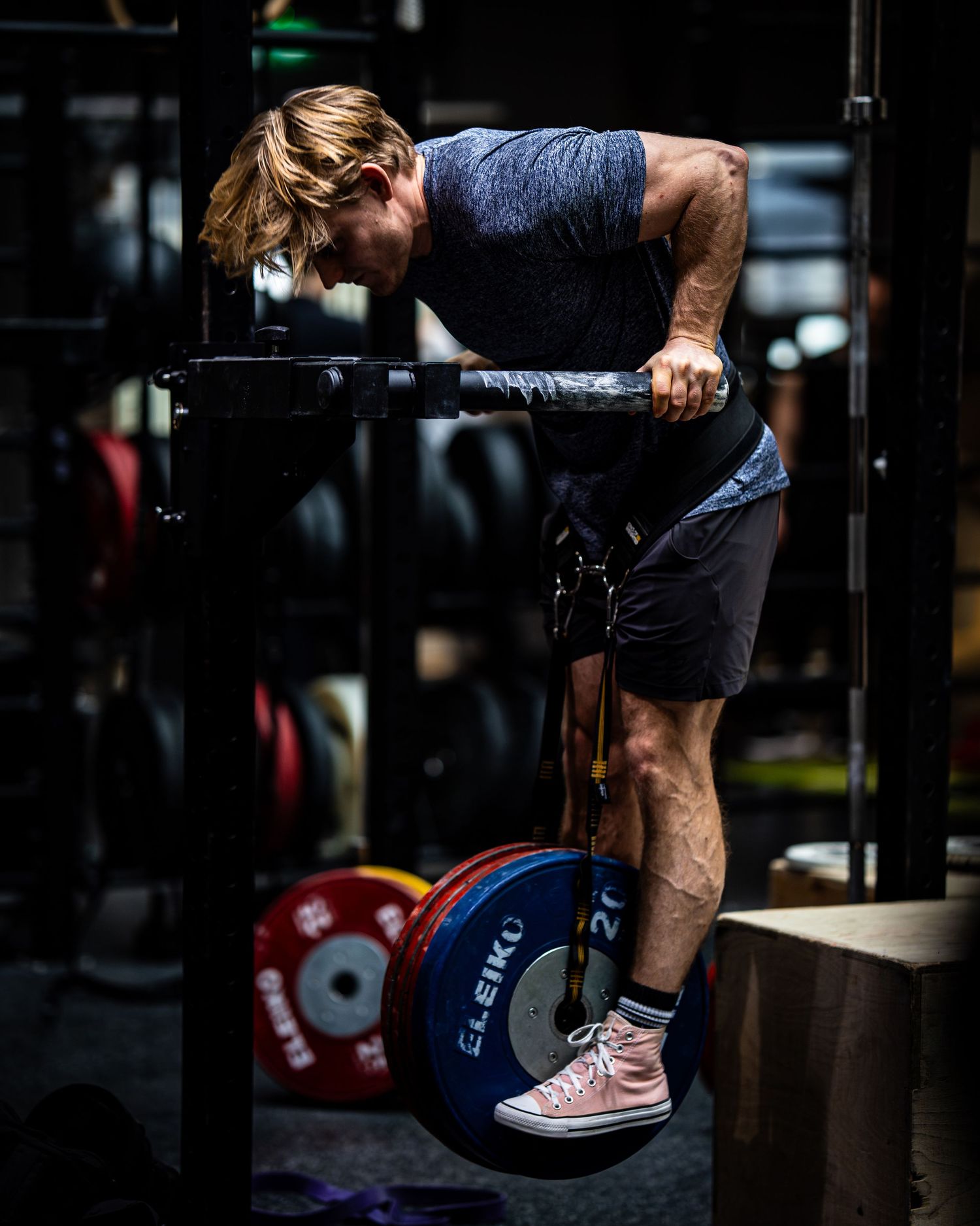 Athlete performs assisted pull-up with weight plate in CrossFit gym environment.