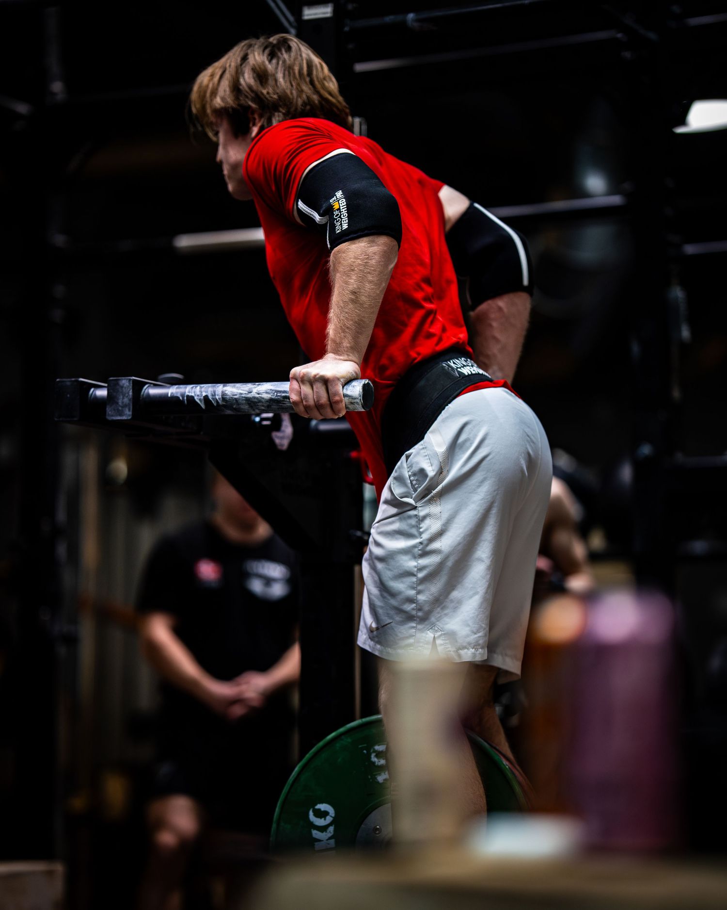 Athlete in red and white attire performing assisted dips in a dimly lit gym environment.