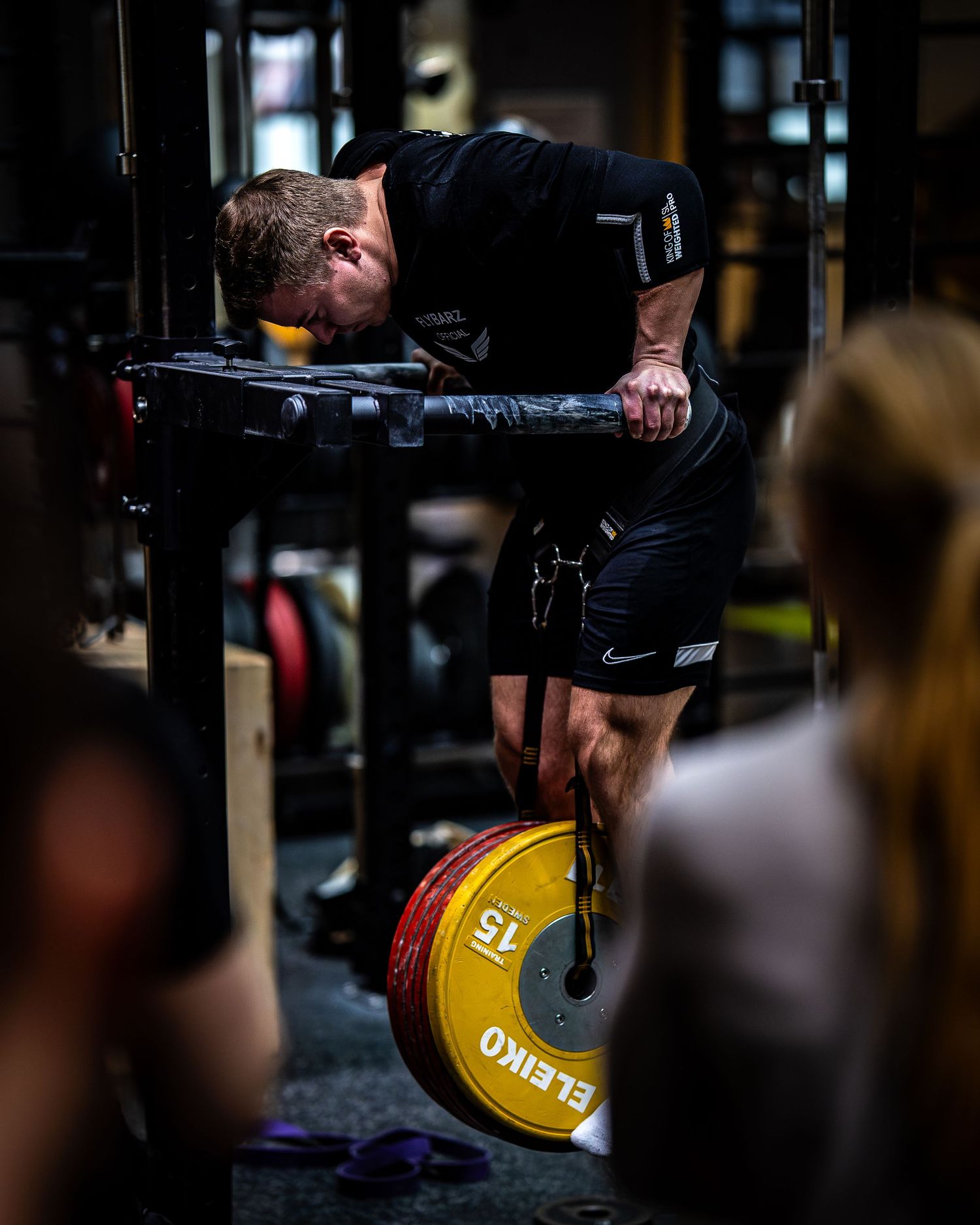 Athlete performing supported upper body exercise in dark gym with yellow Eleiko plate visible below.