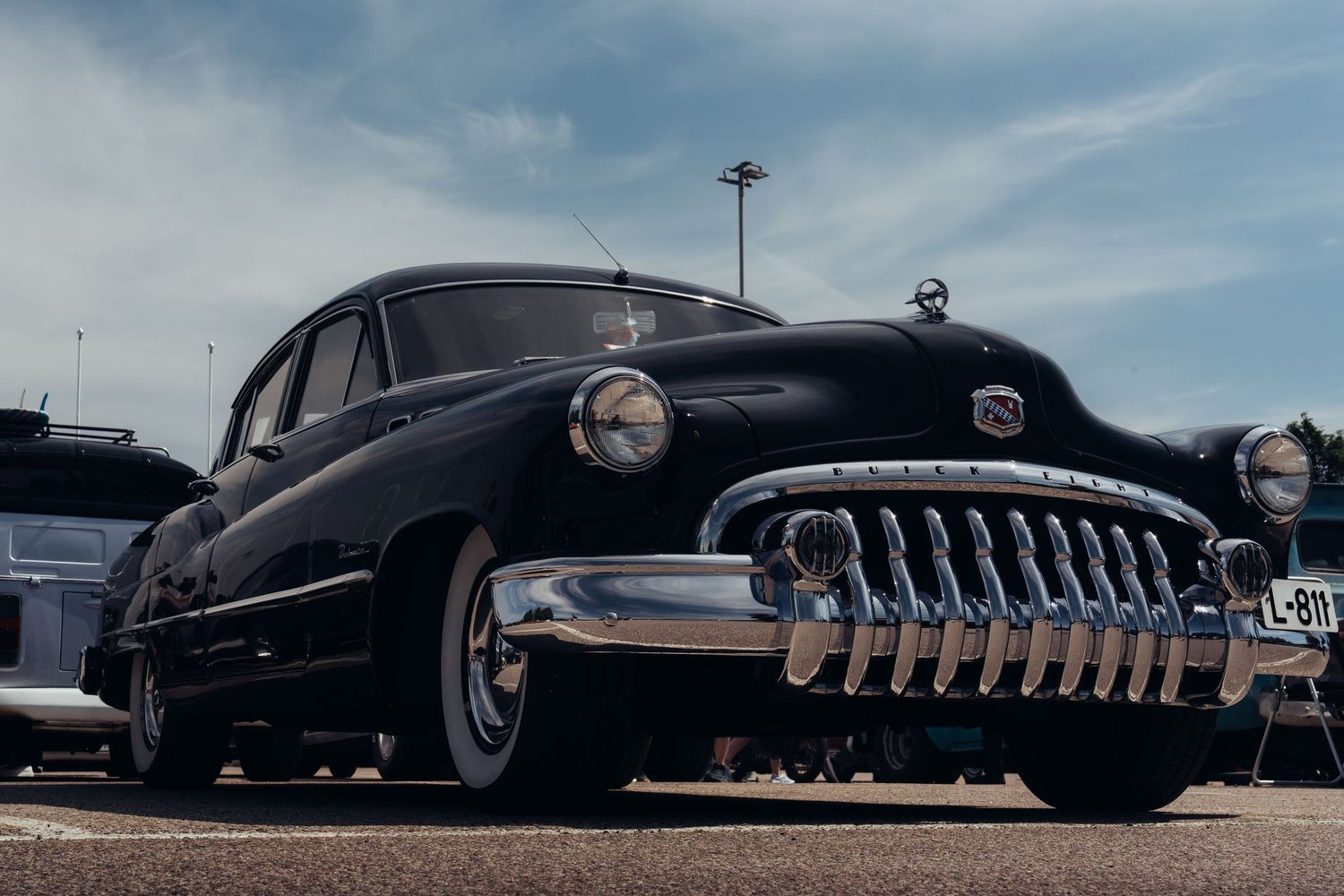 Low angle view of classic American car front grilles lined up in a row against a cloudy blue sky.