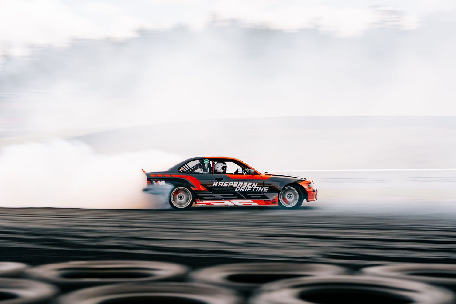 Red sports car drifting on track creating smoke trails during a professional motorsport competition event.