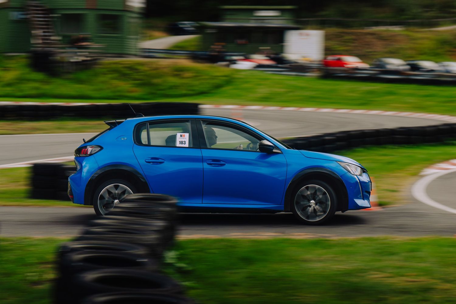 A line of cars parked along a curving road with lush green trees and foliage in the background.