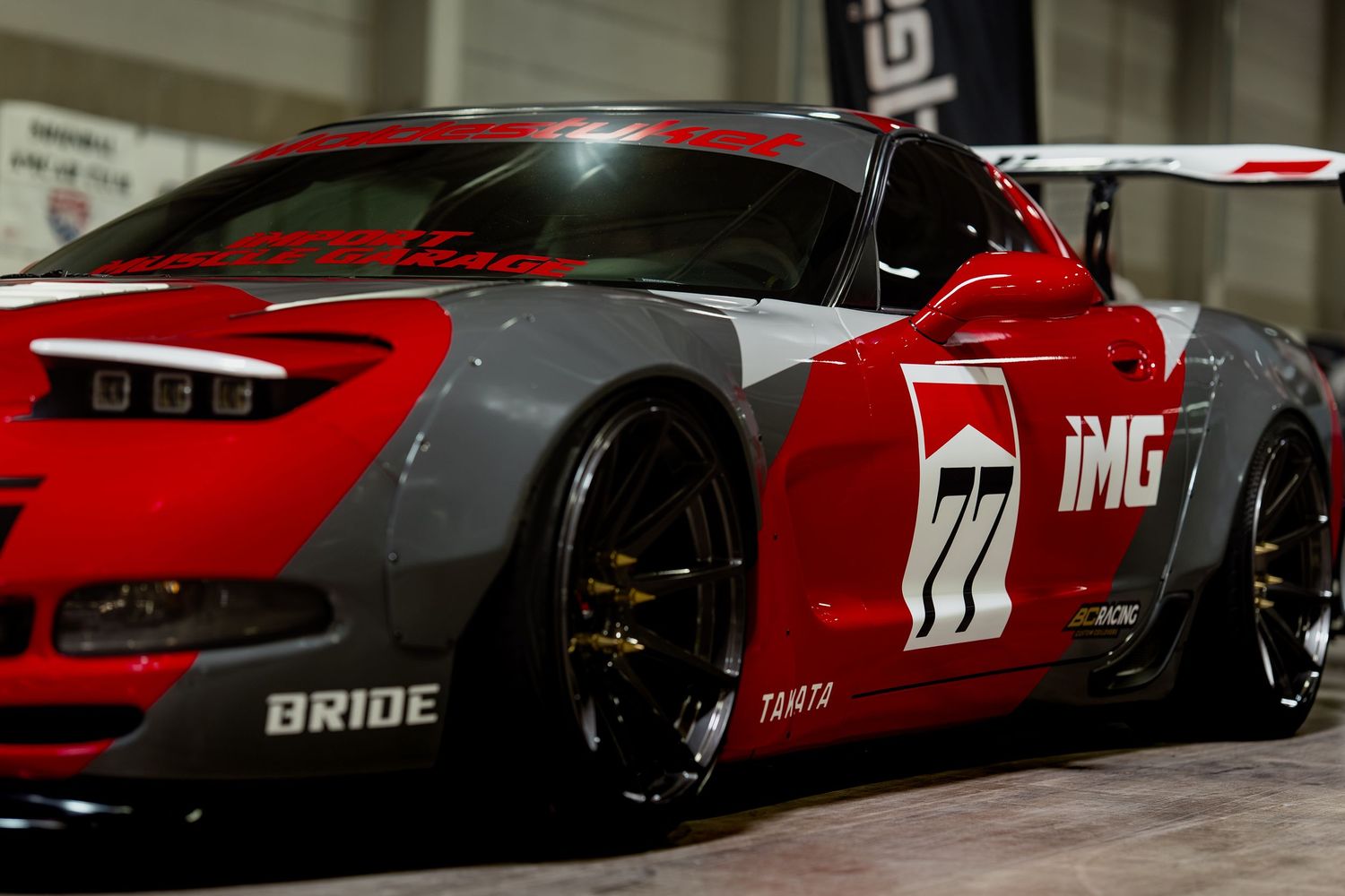 Red and grey race car with IMC branding and wide body kit shown from rear quarter view.