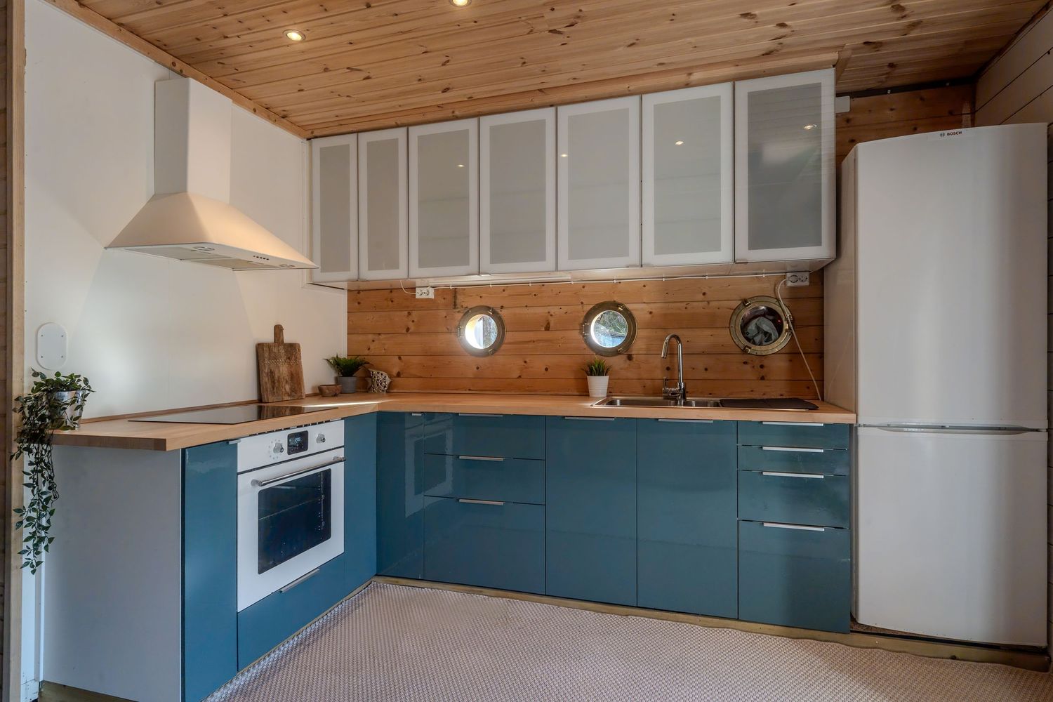 Modern kitchen featuring teal cabinets, wooden walls, and white upper storage with recessed lighting.