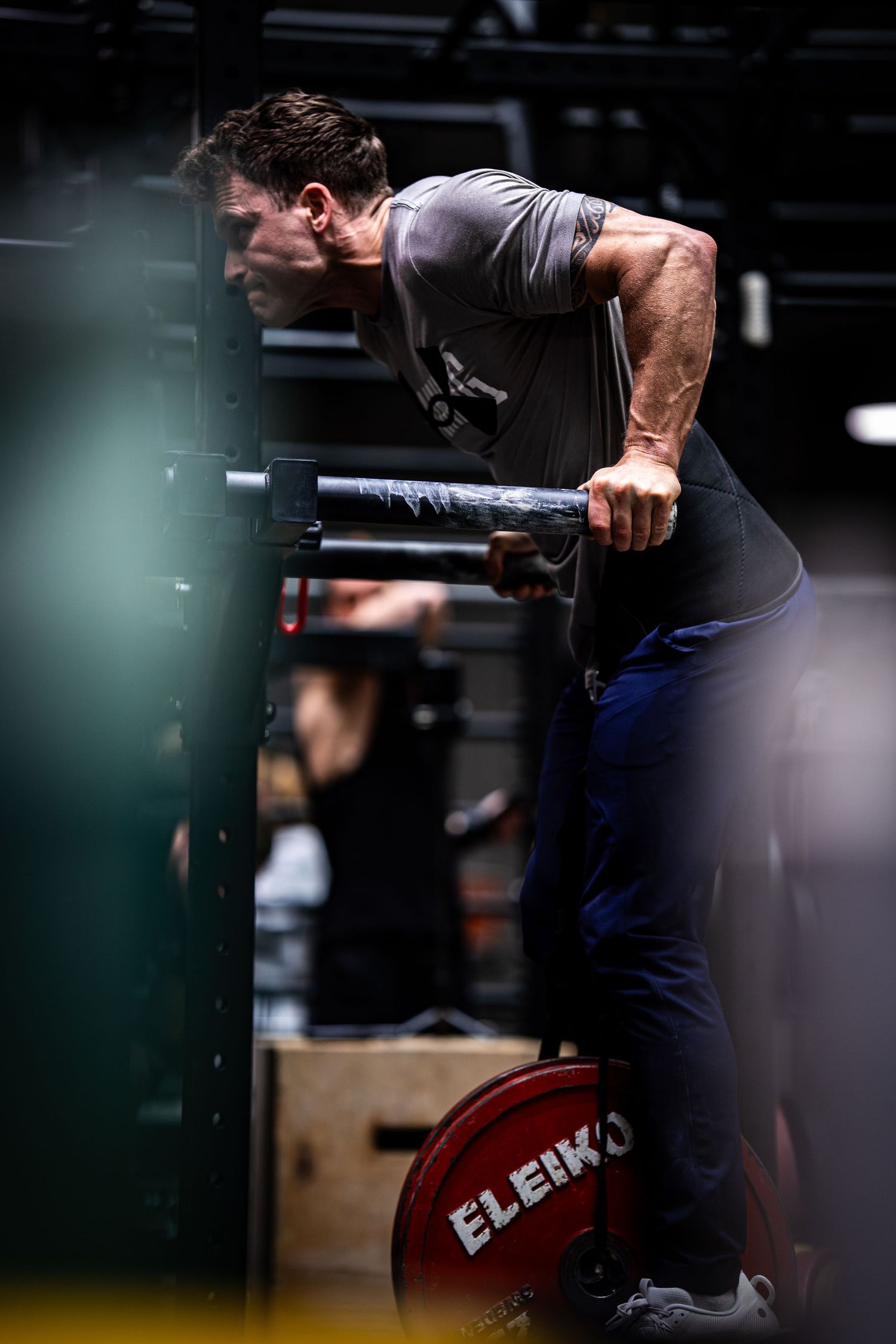 Athletic figure executes dip exercise on parallel bars in dimly lit gym environment.
