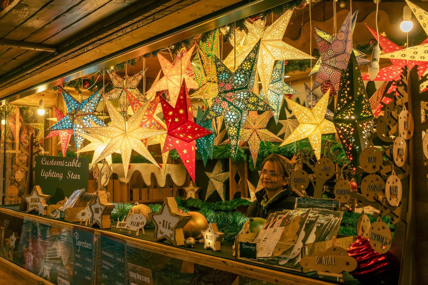 Illuminated paper star lanterns hang from a wooden ceiling creating a warm, festive holiday atmosphere.