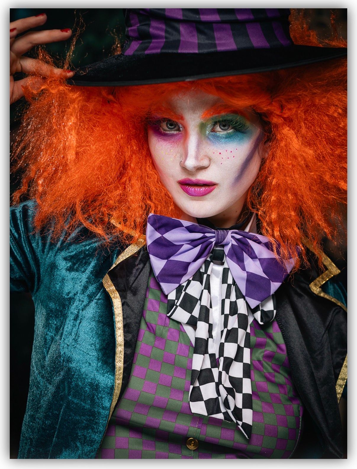 Dramatic portrait featuring bright orange hair, purple and checkered bow tie, and teal velvet costume in Mad Hatter style.