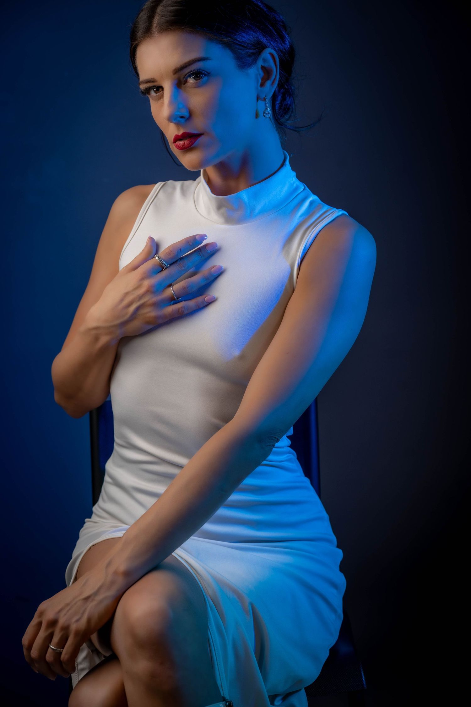 A person in a white sleeveless dress poses against a dark background with dramatic blue lighting creating a moody atmosphere.