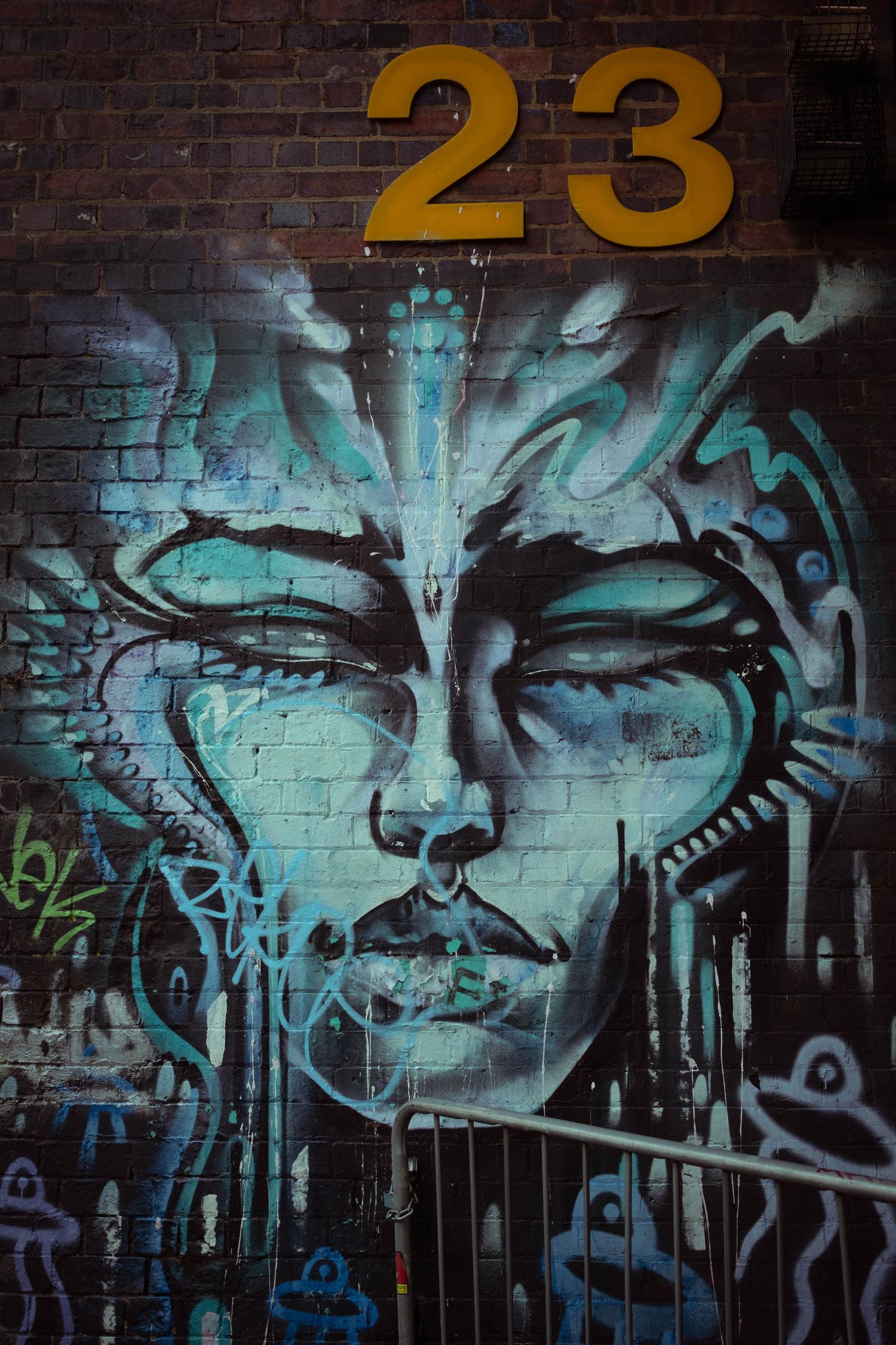 Street art mural on brick wall featuring large turquoise eyes and number 23 with black and yellow accents.