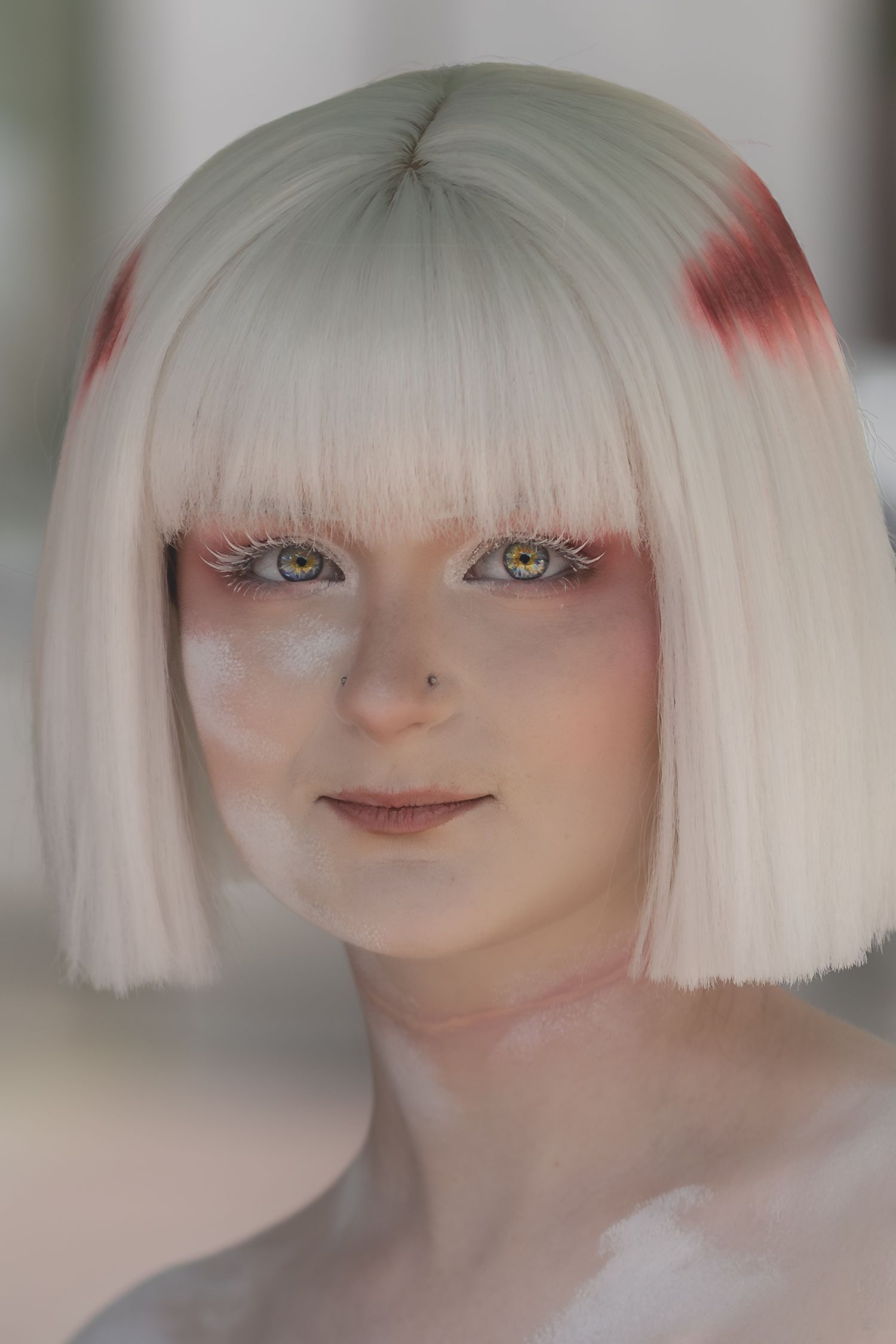Young woman with platinum bob haircut, red-tipped ends, pink eye makeup, and freckles gazing softly at camera.