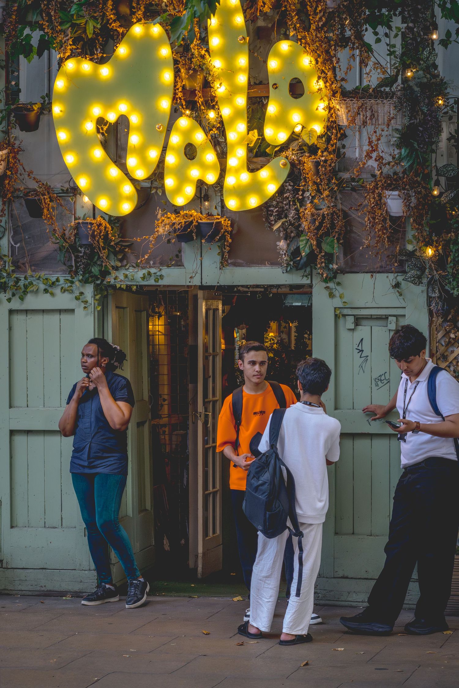 People gathered outside a building at night with decorative yellow string lights creating a warm ambiance.