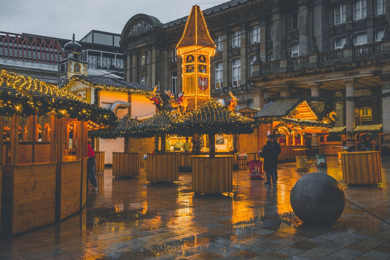 A panoramic cityscape at dusk with glowing orange street lights and historic architecture under moody skies.
