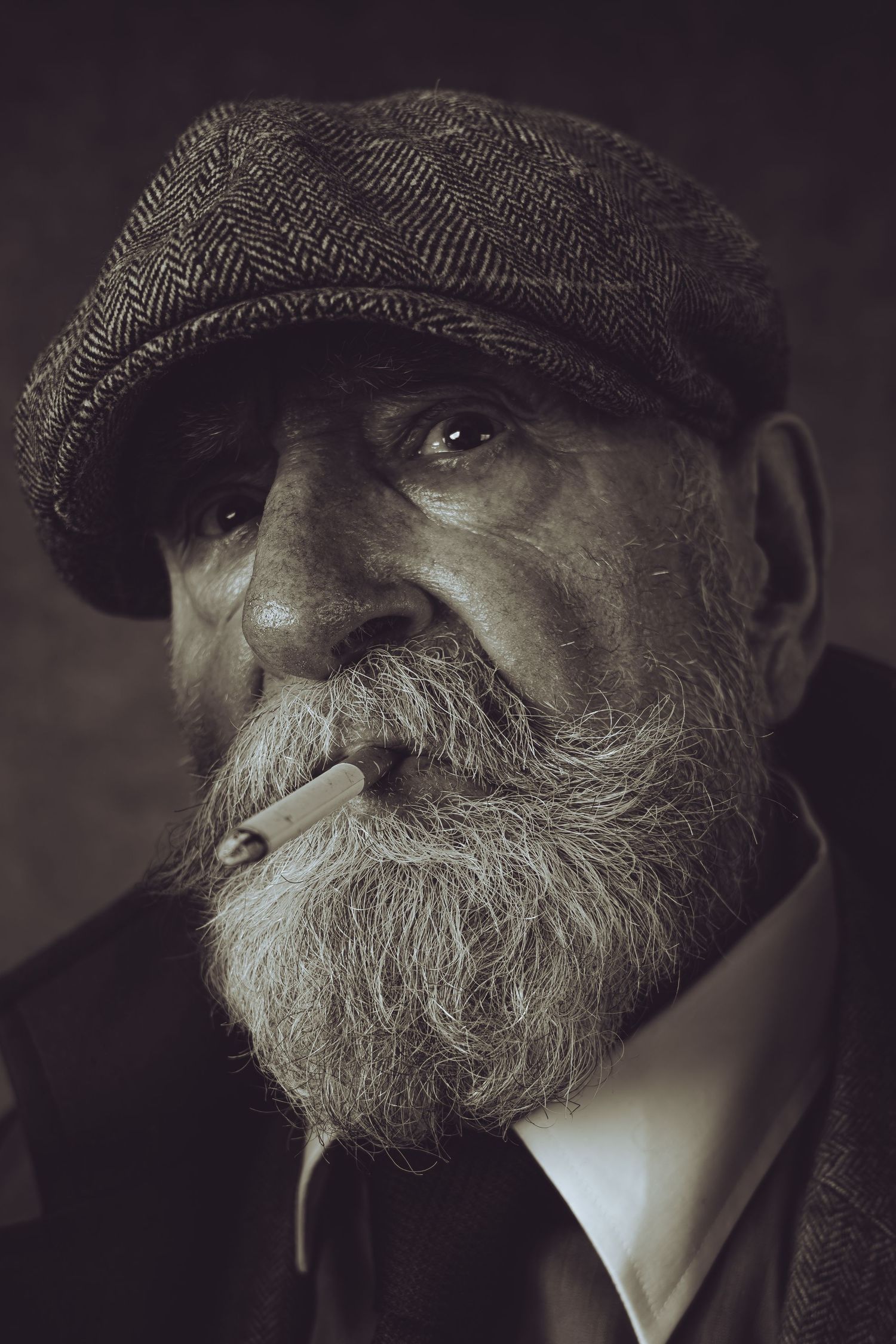Dramatic portrait of bearded elder wearing flat cap and suit in moody lighting.