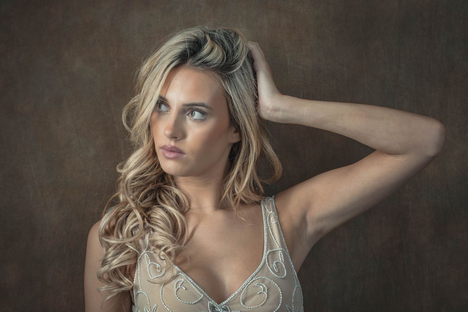 Artistic portrait featuring wavy blonde hair and white lace top against dark moody background.