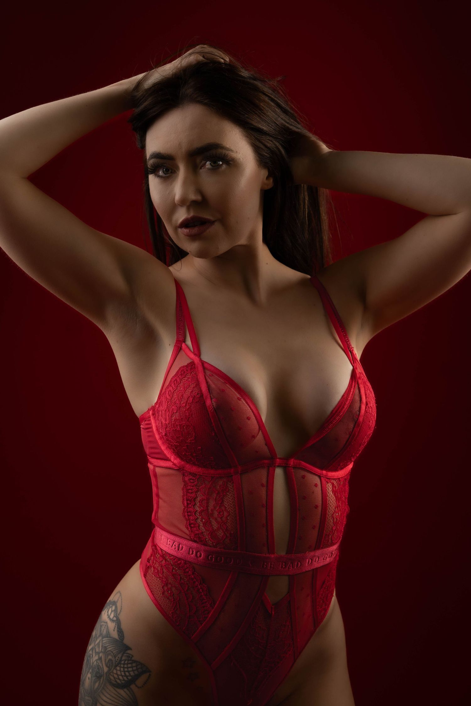 A figure in red lace lingerie poses against a dark burgundy background with dramatic lighting and shadows.