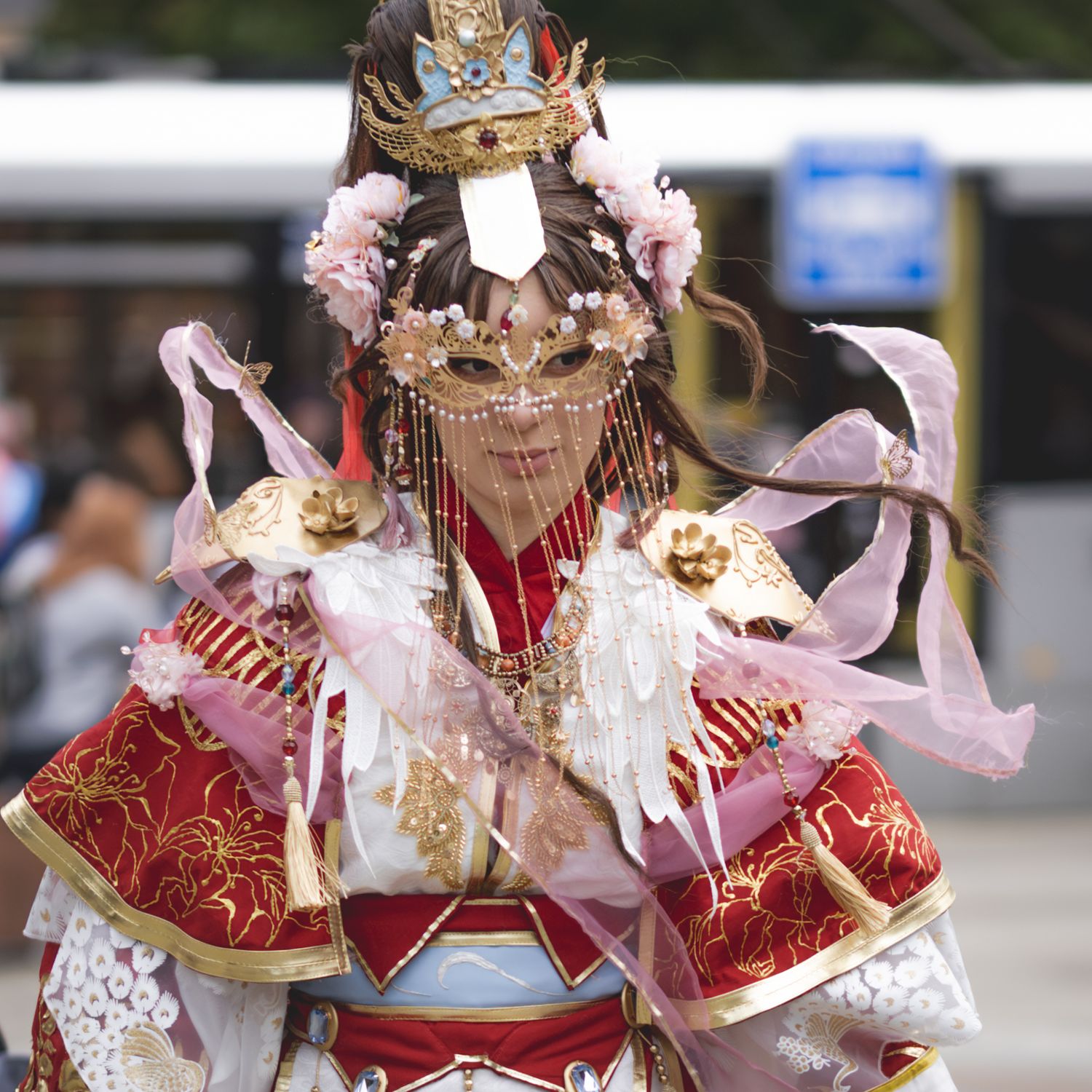 Cosplayer wearing ornate red and gold costume with decorative mask and matching accessories at a convention event.