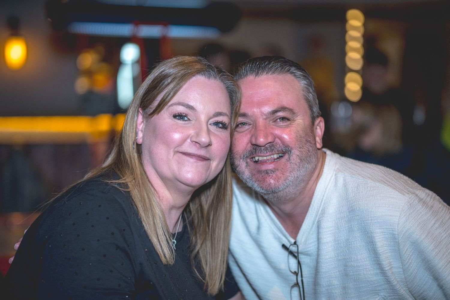 A smiling couple poses cheek to cheek in a warmly lit bar setting.