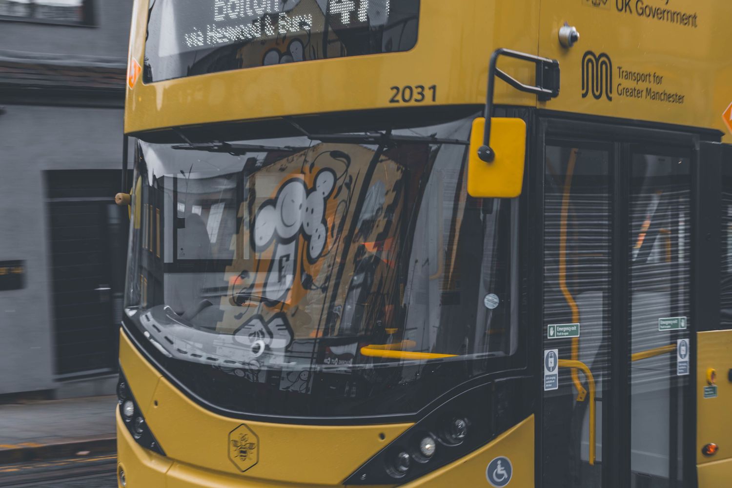 Yellow city buses line up at a transit station with reflective windows and modern architecture visible in the background.