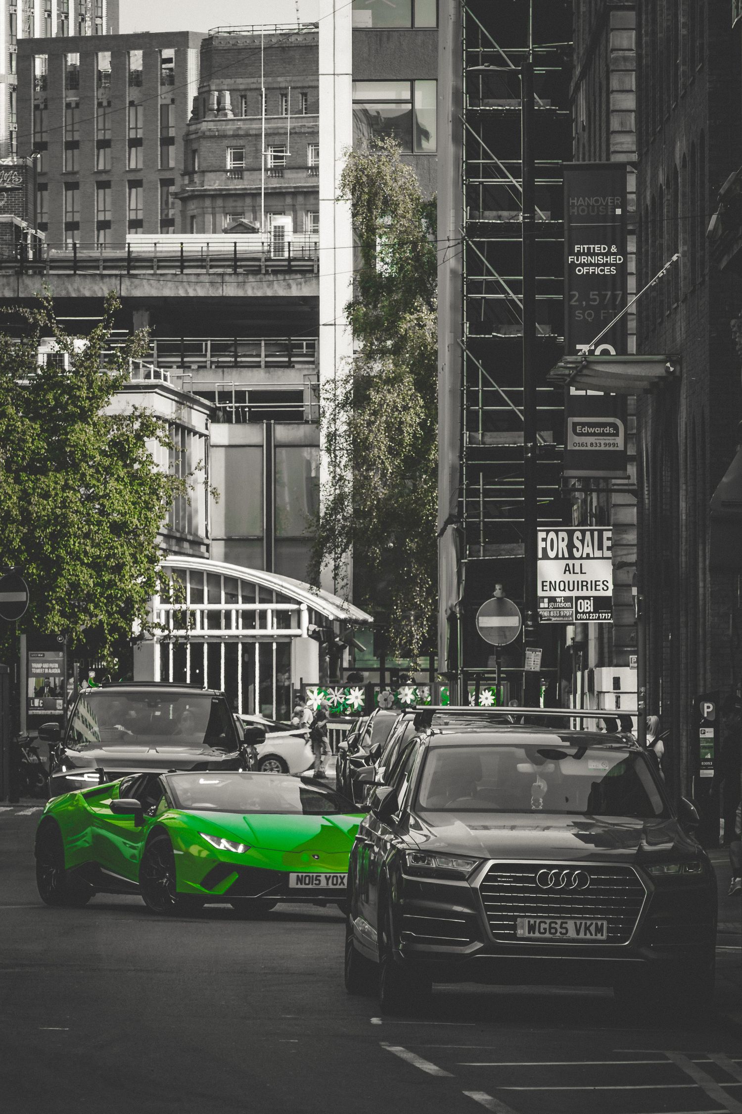 A bright green sports car stands out against a black and white urban street scene with buildings and parked cars.