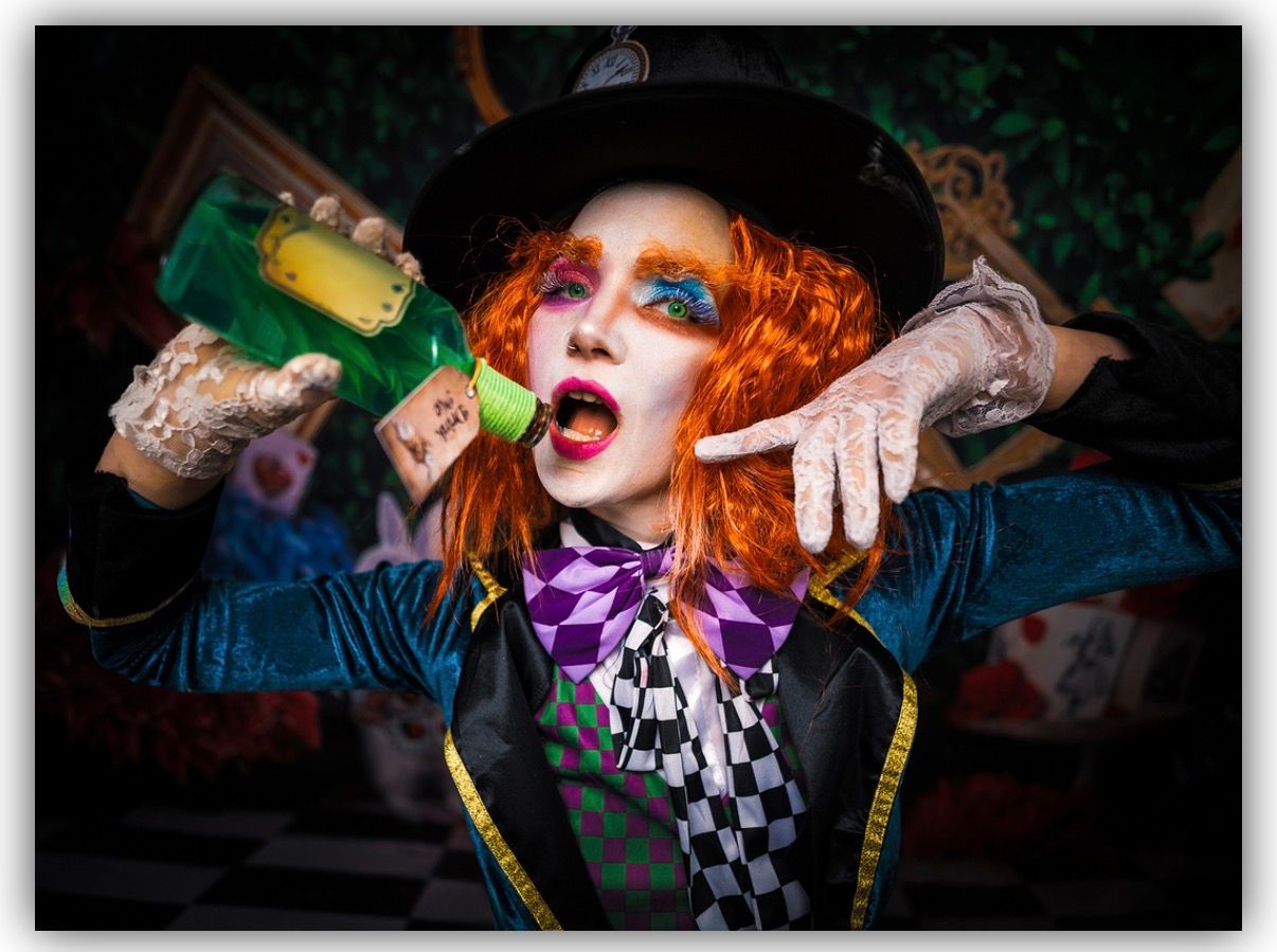 Performer with bright orange hair and dramatic makeup sings passionately on stage during a theatrical performance.