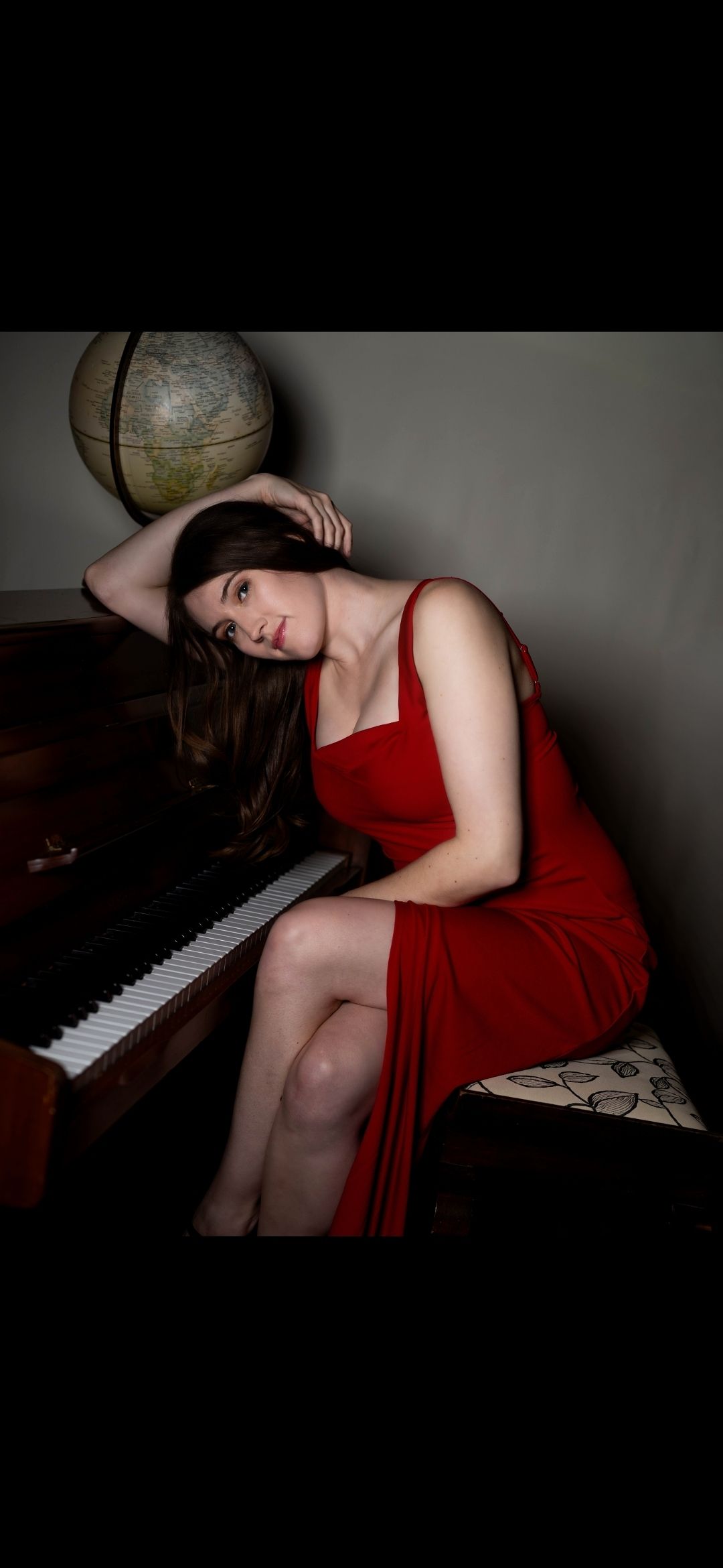 Woman in red dress posing elegantly by a grand piano with a vintage globe in the background.