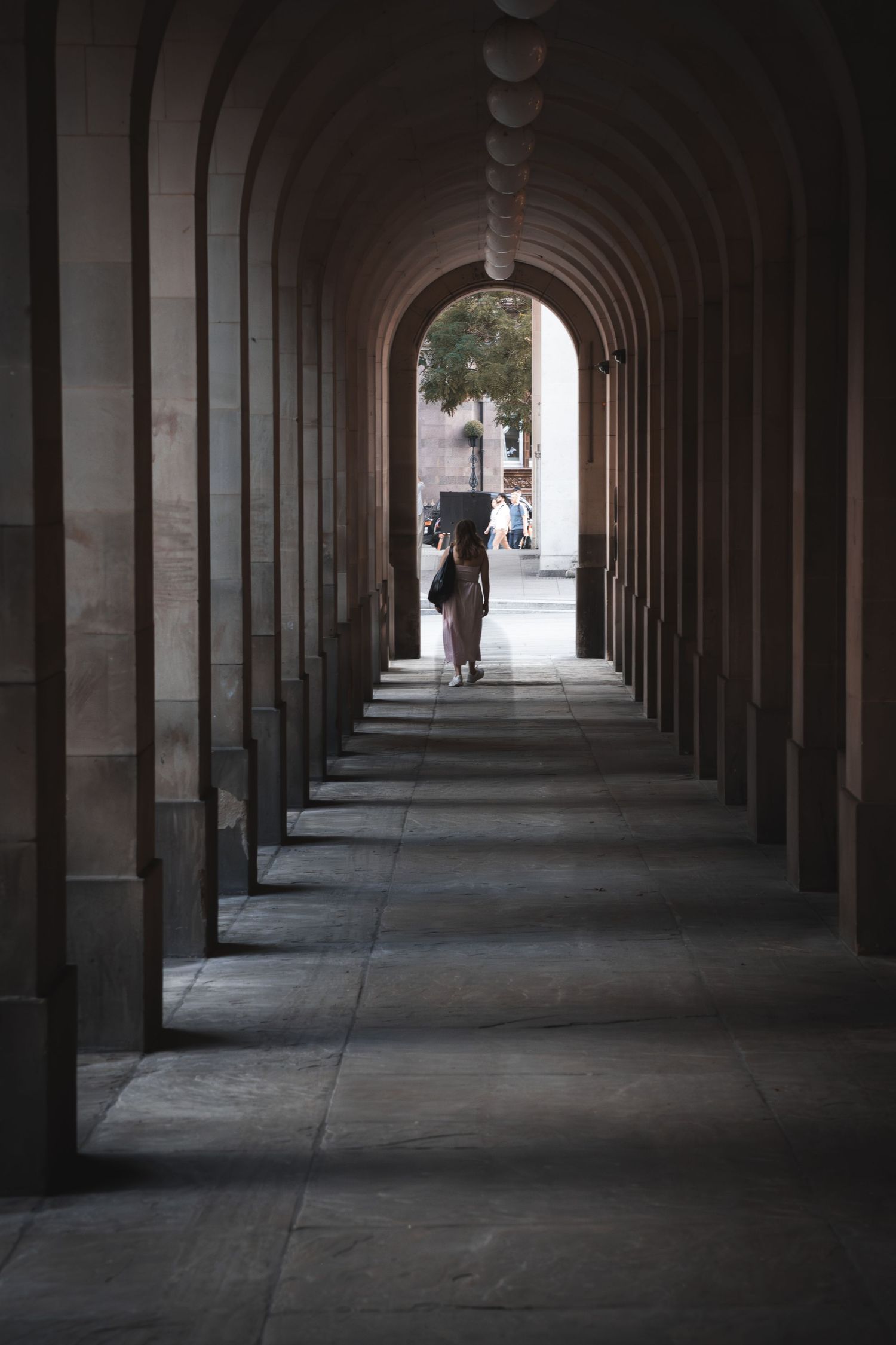 Long covered colonnade with repeating stone archways creating dramatic perspective and shadows.