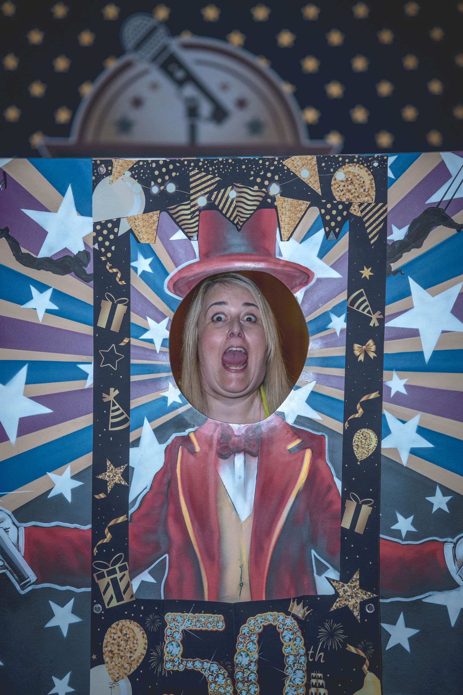 Woman posing through a colorful 50th birthday party photo booth frame with circus ringmaster design.