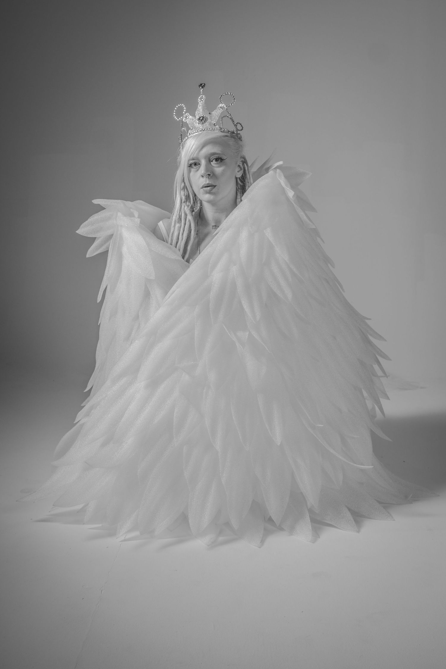 A figure in an ethereal white feathered dress poses dramatically in a series of black and white photographs.