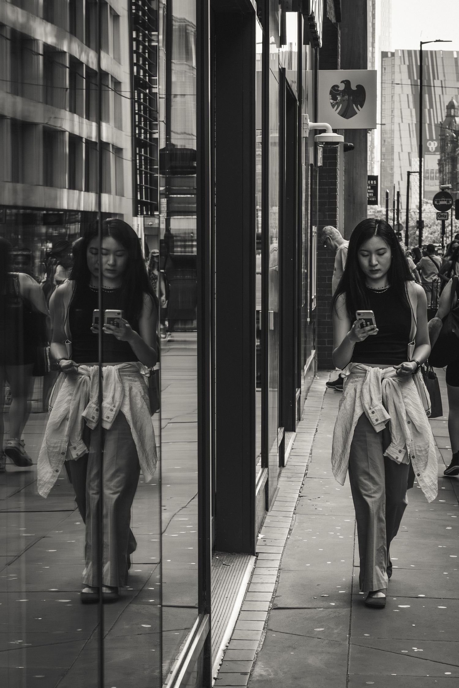 Urban street scene with reflective glass windows and pedestrians walking along a modern building exterior.