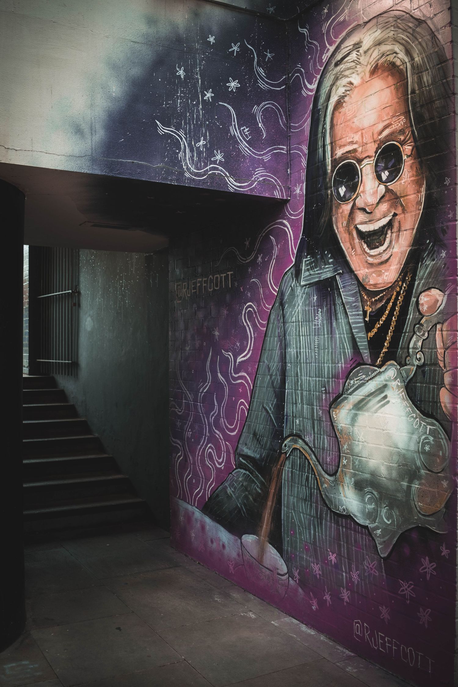 Dark stairwell with vibrant street art mural featuring a figure in sunglasses and suit against purple smoky background.