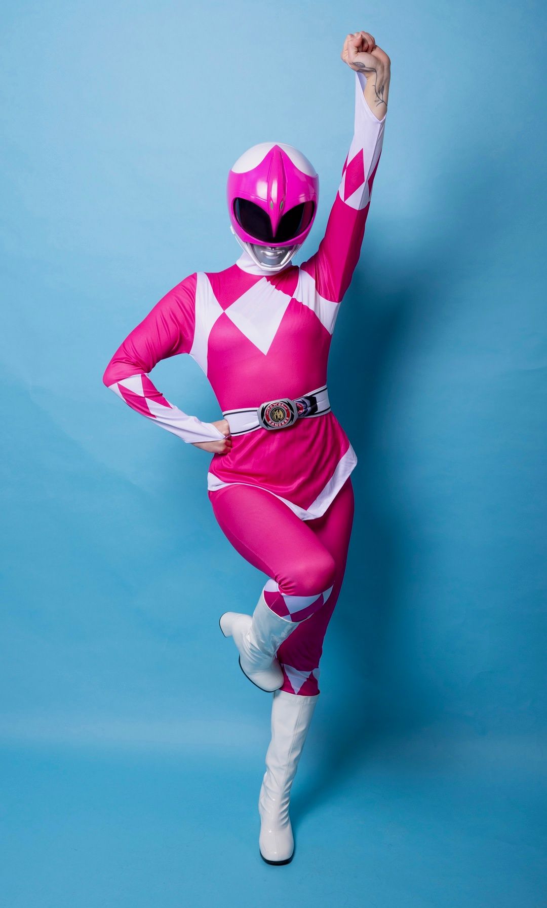 Person in Pink Power Ranger costume with helmet, striking a heroic pose against a blue background.
