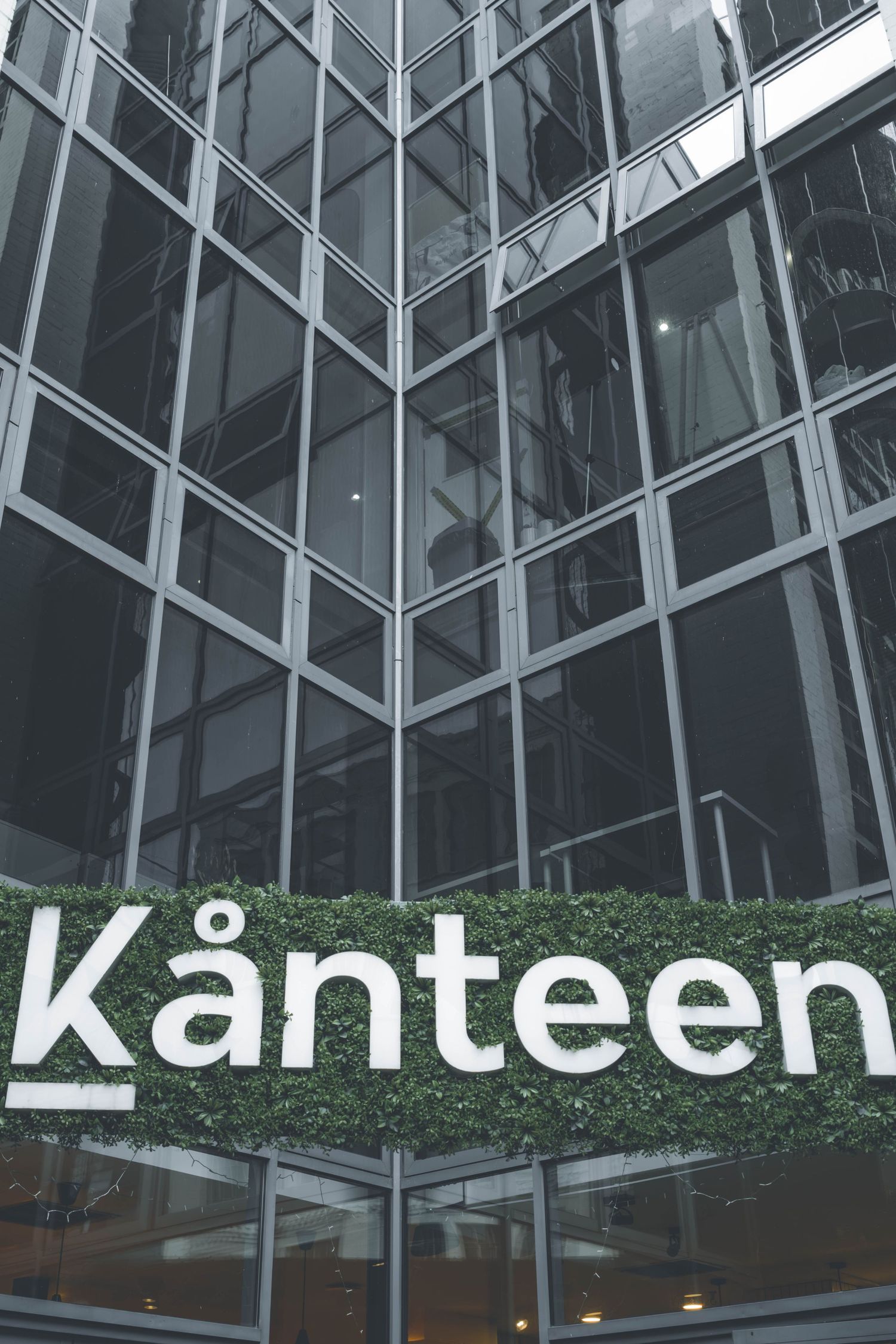Modern office building exterior with glass windows and Kanteen signage mounted on a wall with greenery.