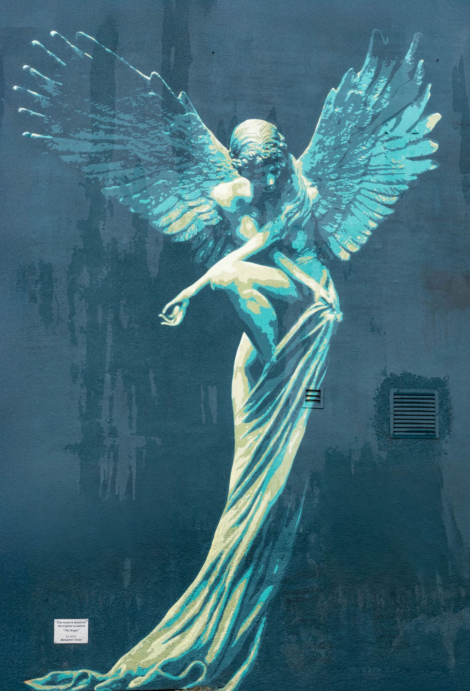 A luminous angel statue with turquoise wings stands gracefully against a dark background in ethereal lighting.