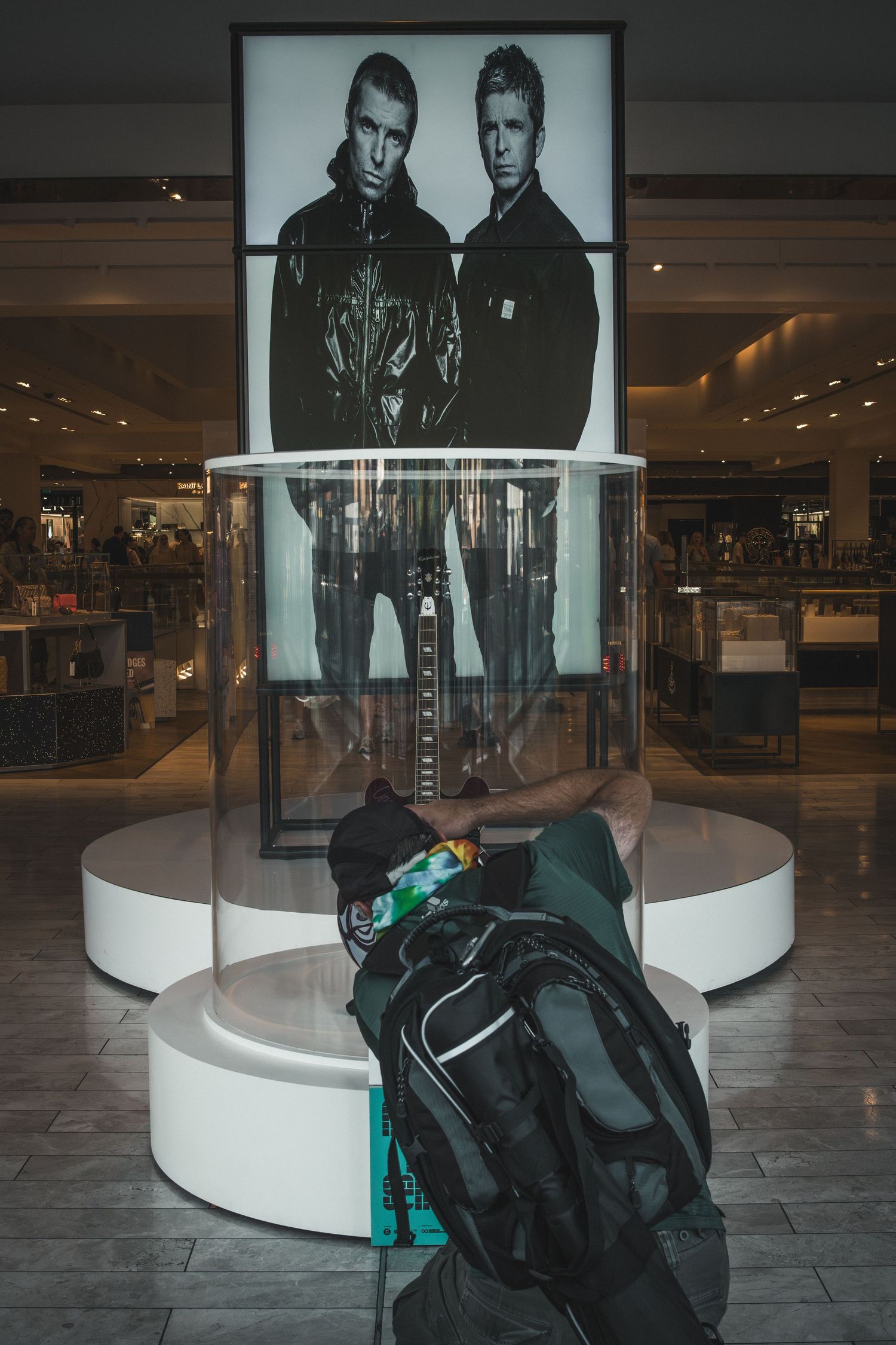 Fashion advertisement display in a modern shopping mall with black backpack placed on white circular platform.