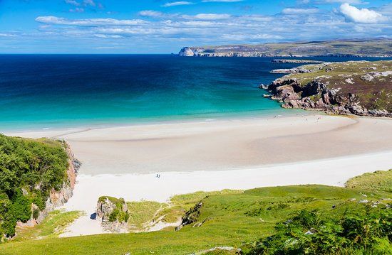 Panoramic view of pristine white sand beaches and turquoise waters along a rugged coastal landscape under blue skies.