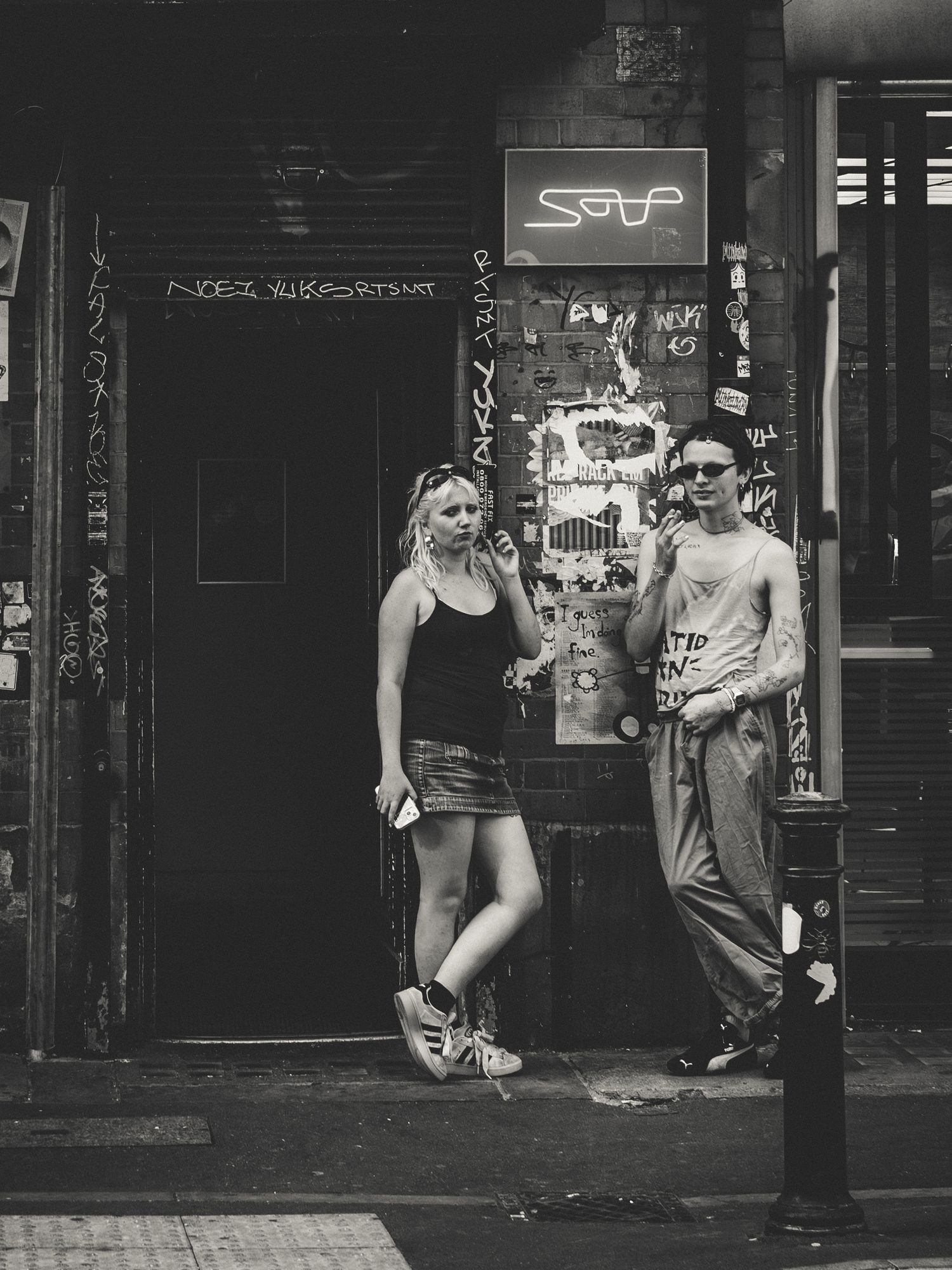 A set of black and white street photography shots showing glimpses of people near urban storefronts and alleyways.