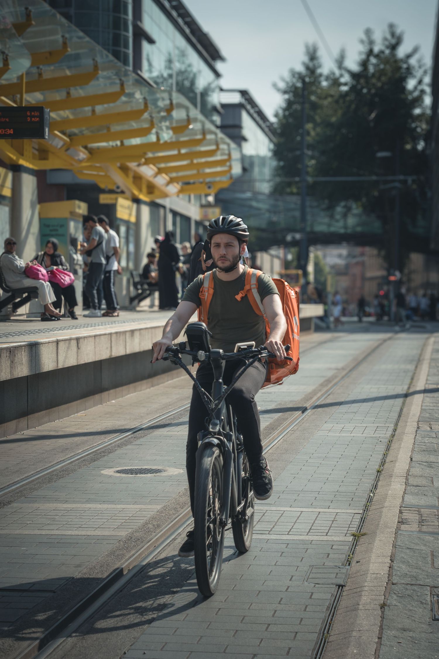 A cyclist rides along a paved path next to yellow overhead structures on a sunny day.