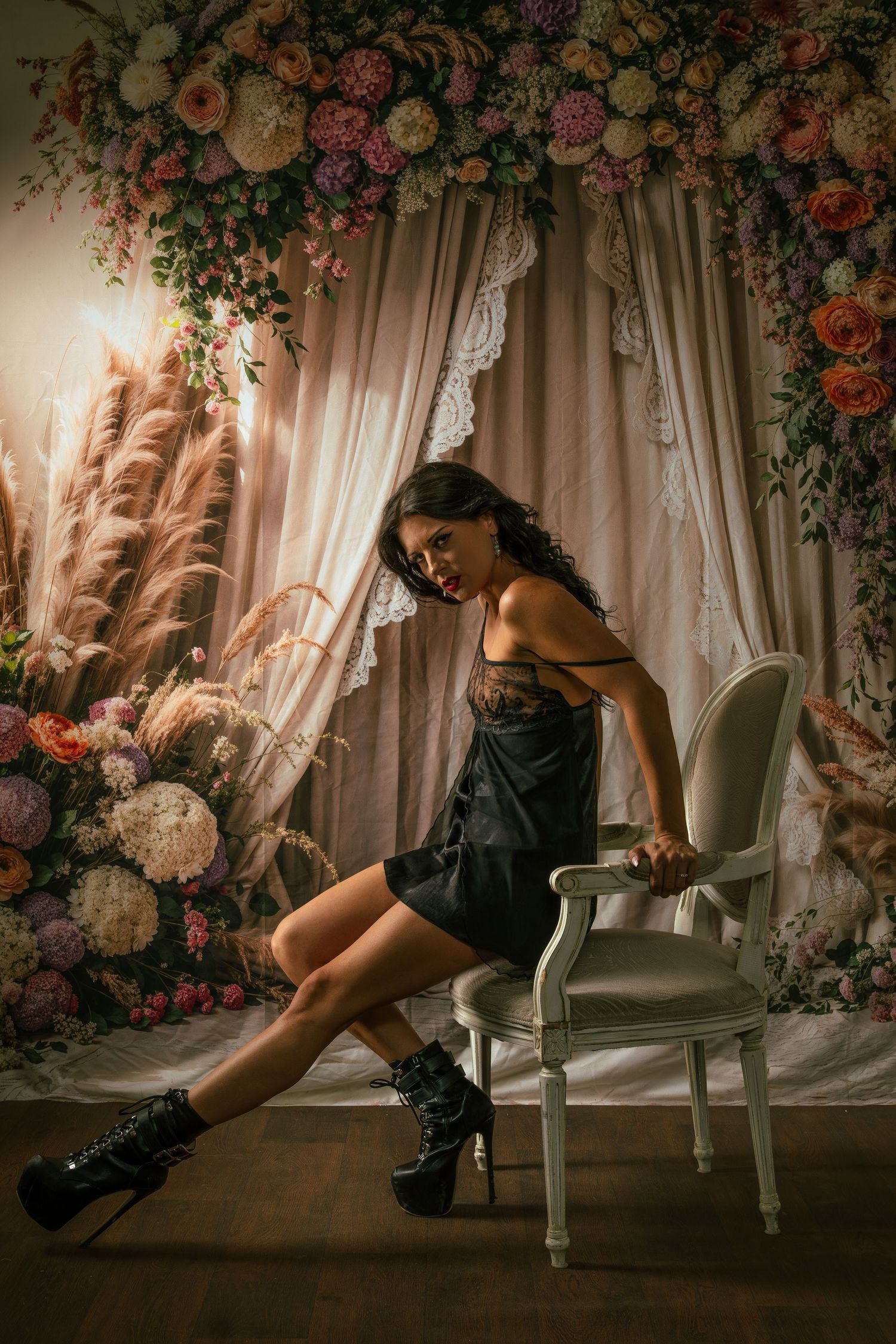 Dramatic boudoir photoshoot with floral backdrop and elegant white chair.