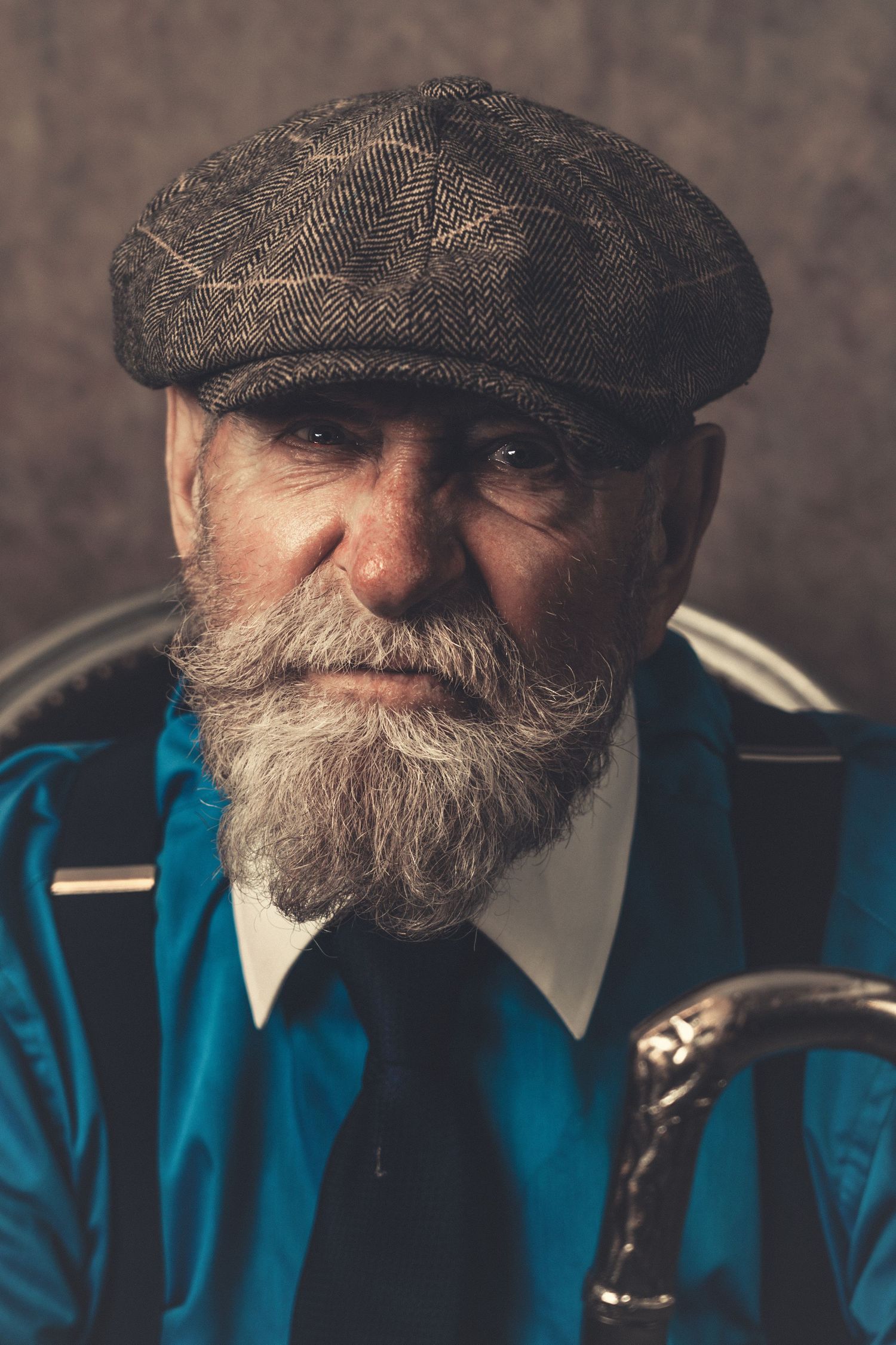 Portrait of distinguished gentleman with white beard wearing flat cap and blue jacket.