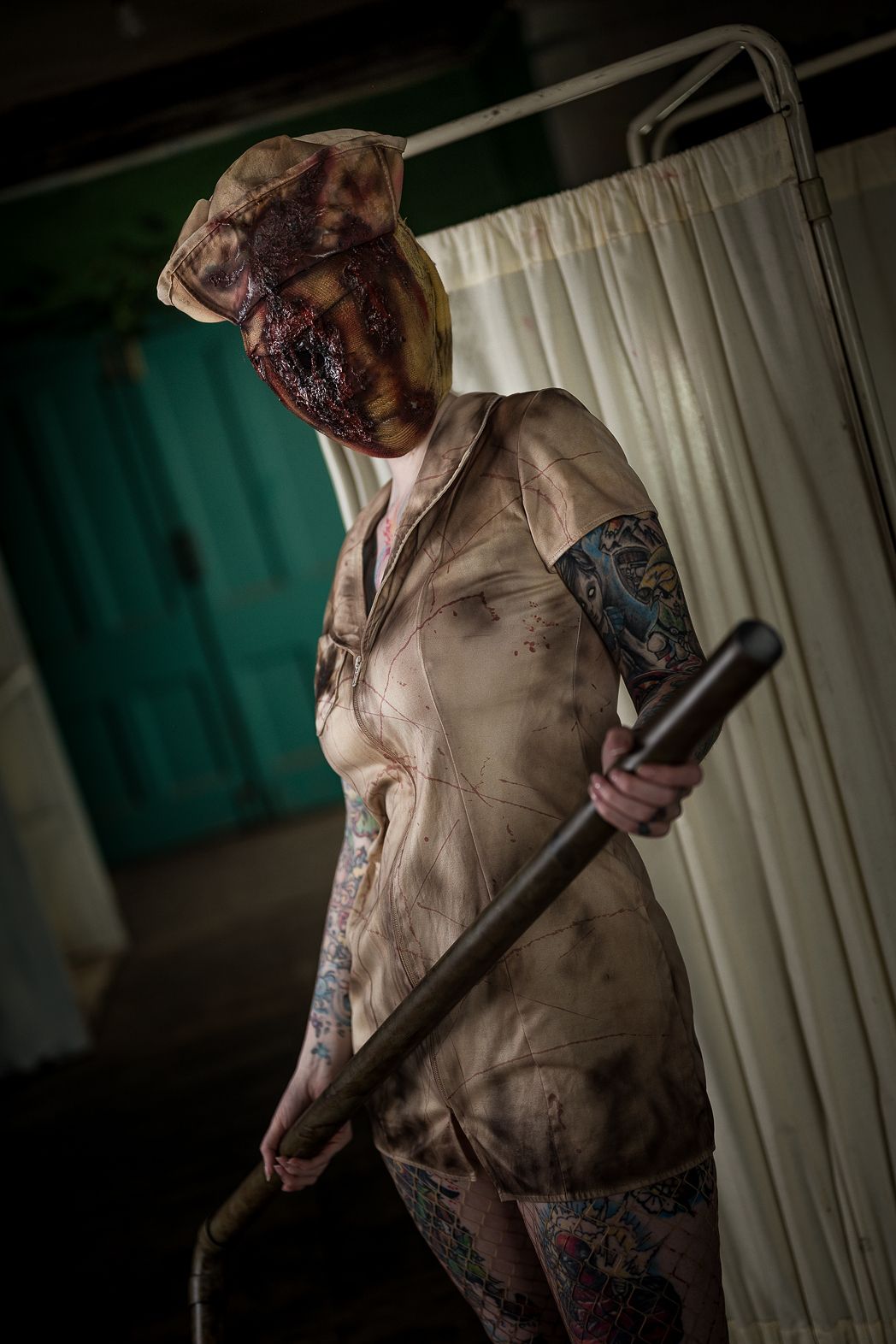 A Silent Hill nurse cosplay costume with distorted mask, tattered uniform, and metal pipe in an abandoned hospital.