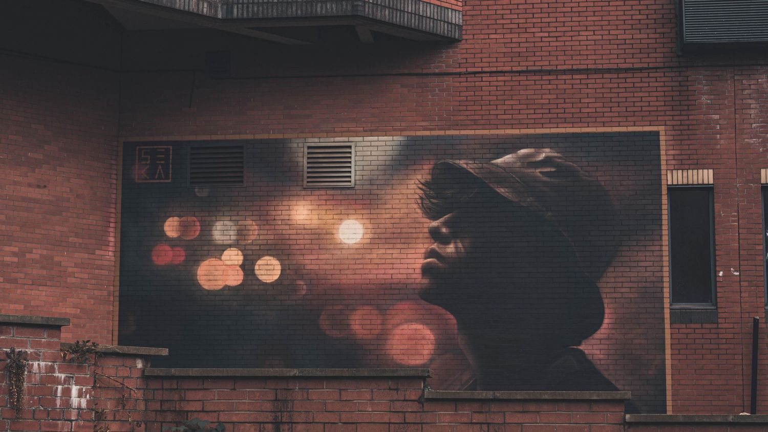 Dark artistic mural on brick wall with silhouette and glowing orange bokeh light effects in urban setting.