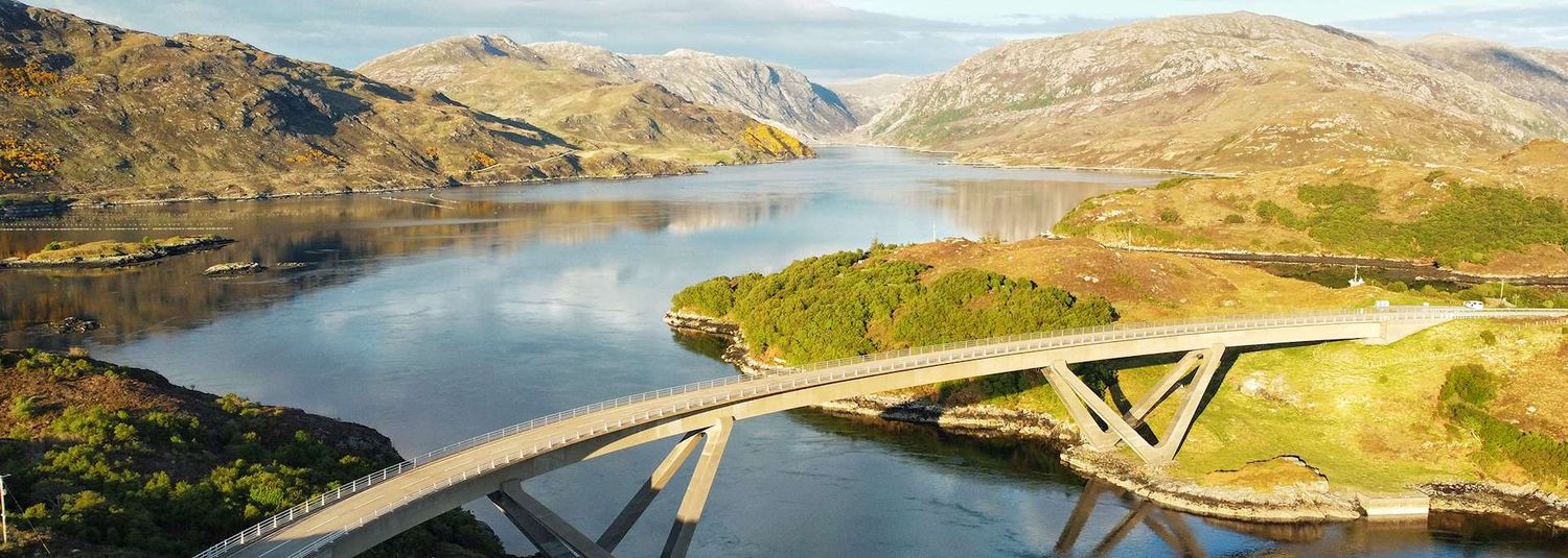 Scenic mountain landscape with winding roads, lakes and bridges stretching across rugged terrain in a remote area.