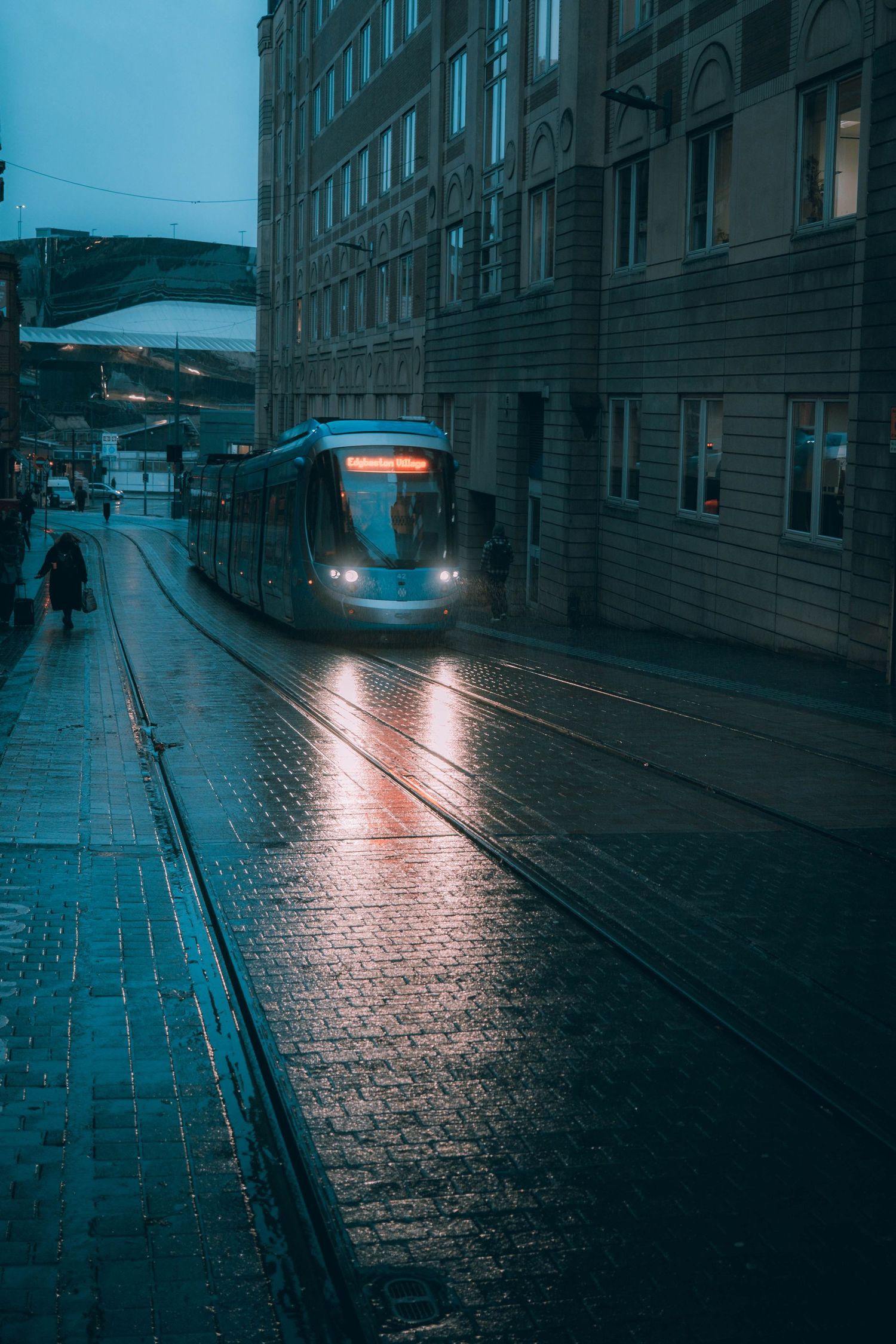 Rainy evening on cobblestone street with wet tram tracks reflecting city lights in moody blue tones.
