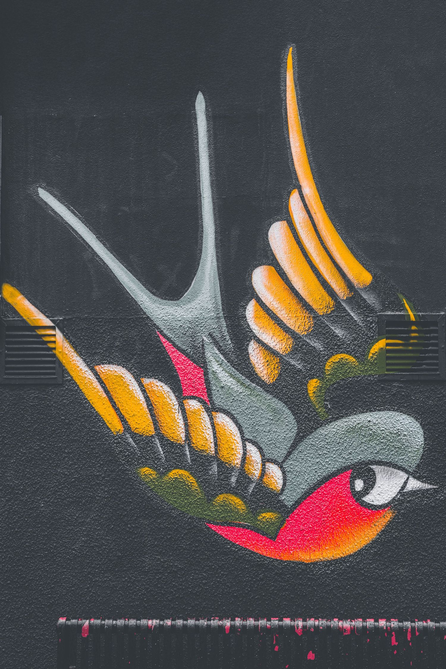 Street art mural on dark wall shows stylized orange and red bird with geometric wing pattern and musical notes.