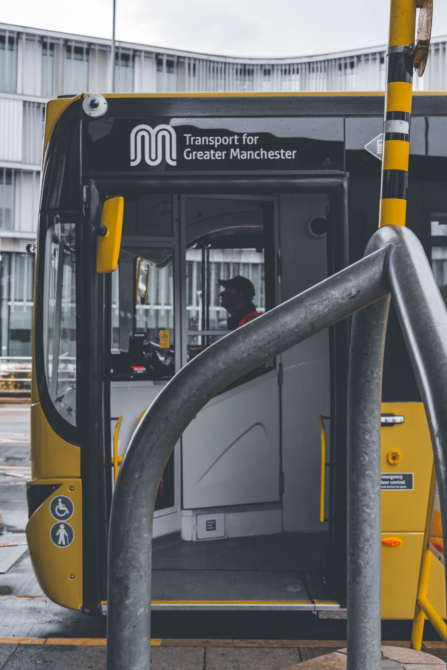 Yellow Transport for Greater Manchester bus door entrance with metal safety barriers at a station stop.
