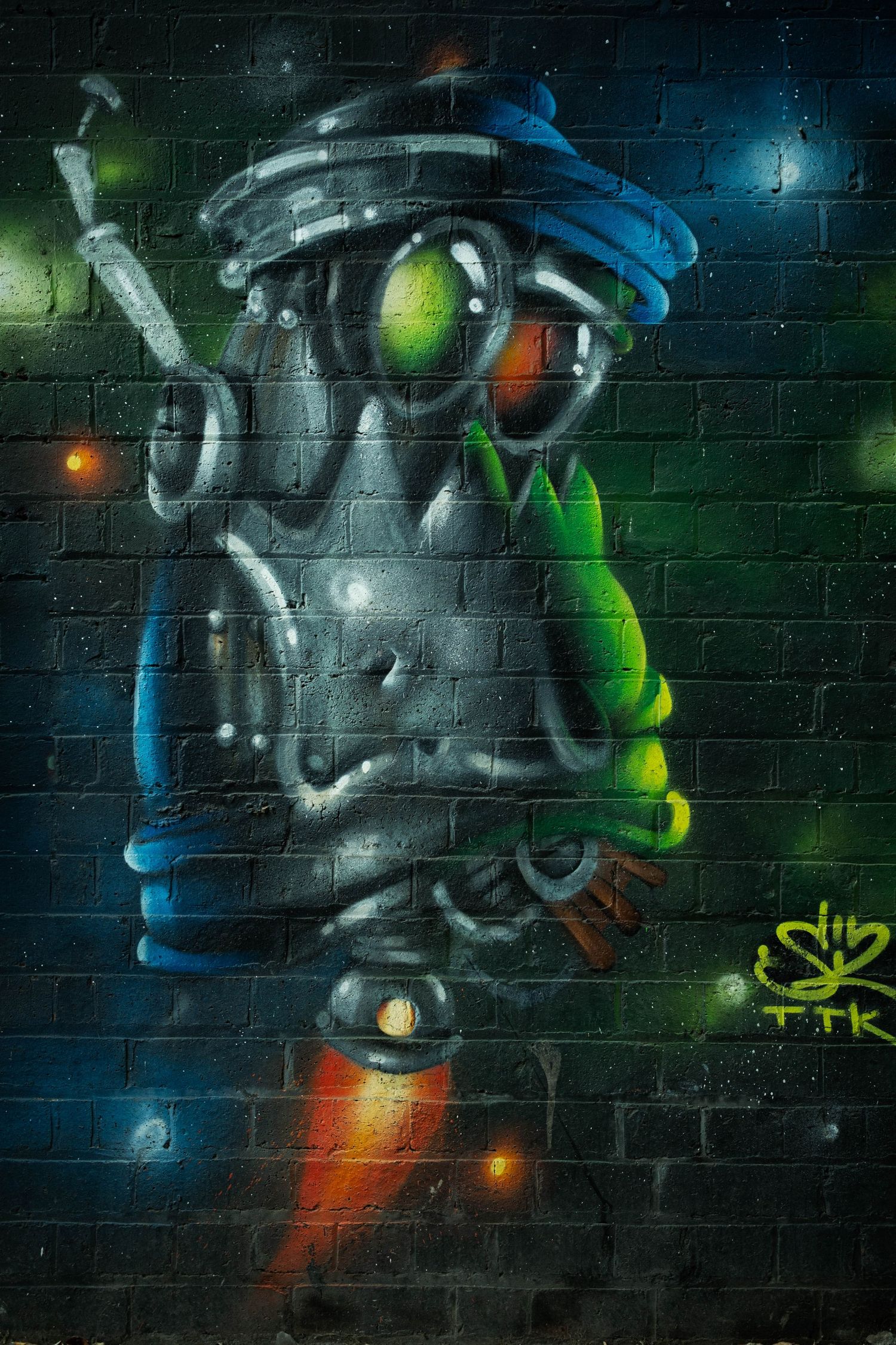 Vibrant street art mural featuring a futuristic robot character in green and blue tones against a dark brick wall.